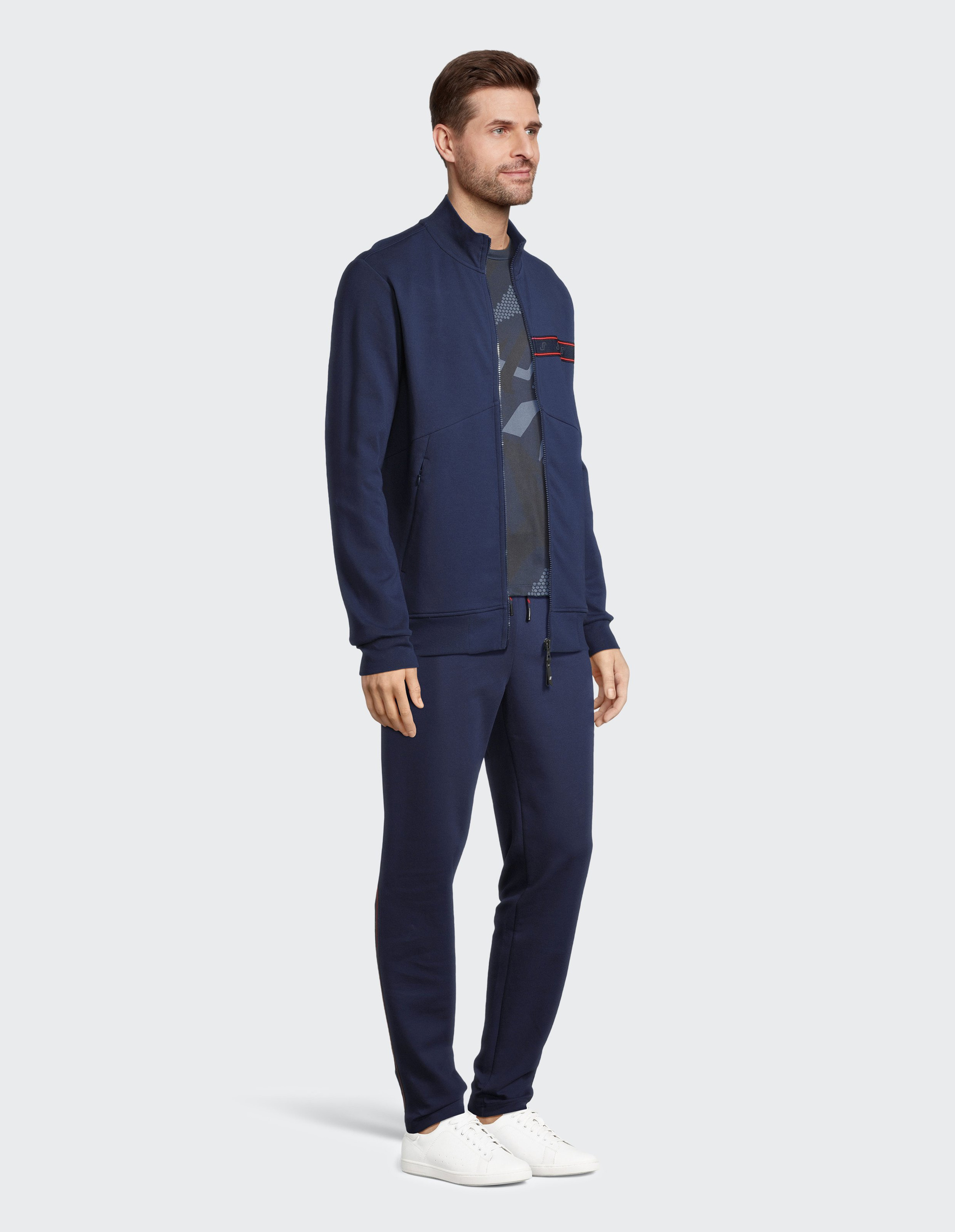 Dunkelblaue Jacke mit Reißverschluss, Stehkragen und einem dezenten roten Streifen über der Brust mit Logos verziert.
