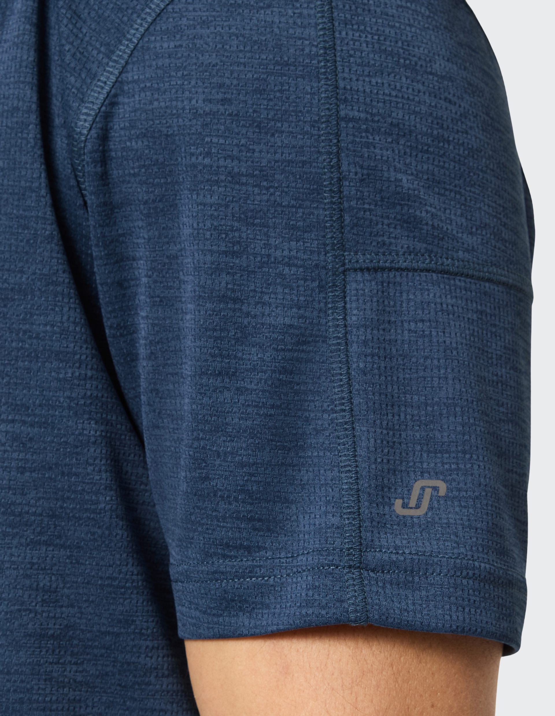 Dunkelblaues, texturiertes T-Shirt mit kurzem Ärmel und dezentem Logo am Saum, getragen von einer Person mit heller Haut.