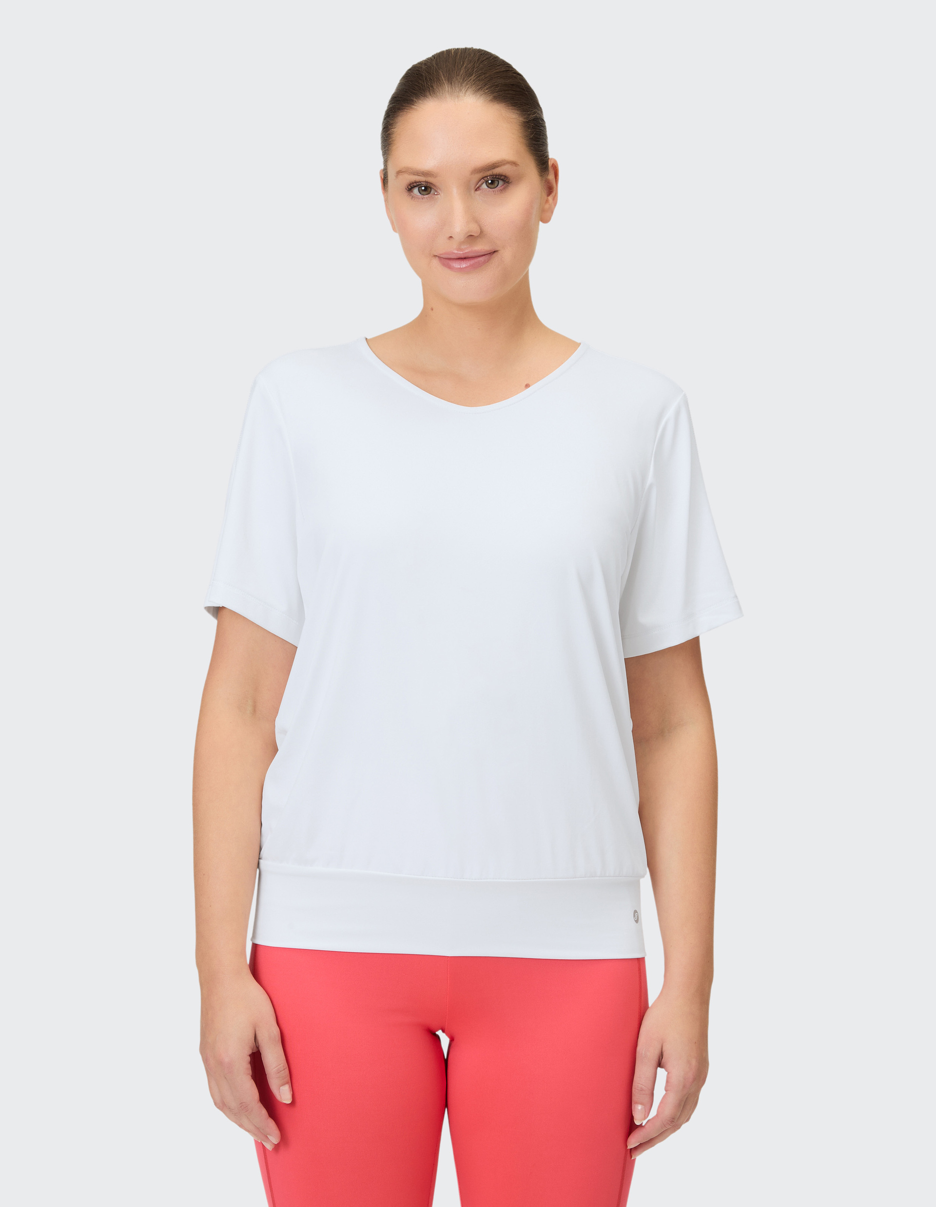 Eine Frau trägt ein weißes T-Shirt mit V-Ausschnitt und eine korallenrote Leggings.