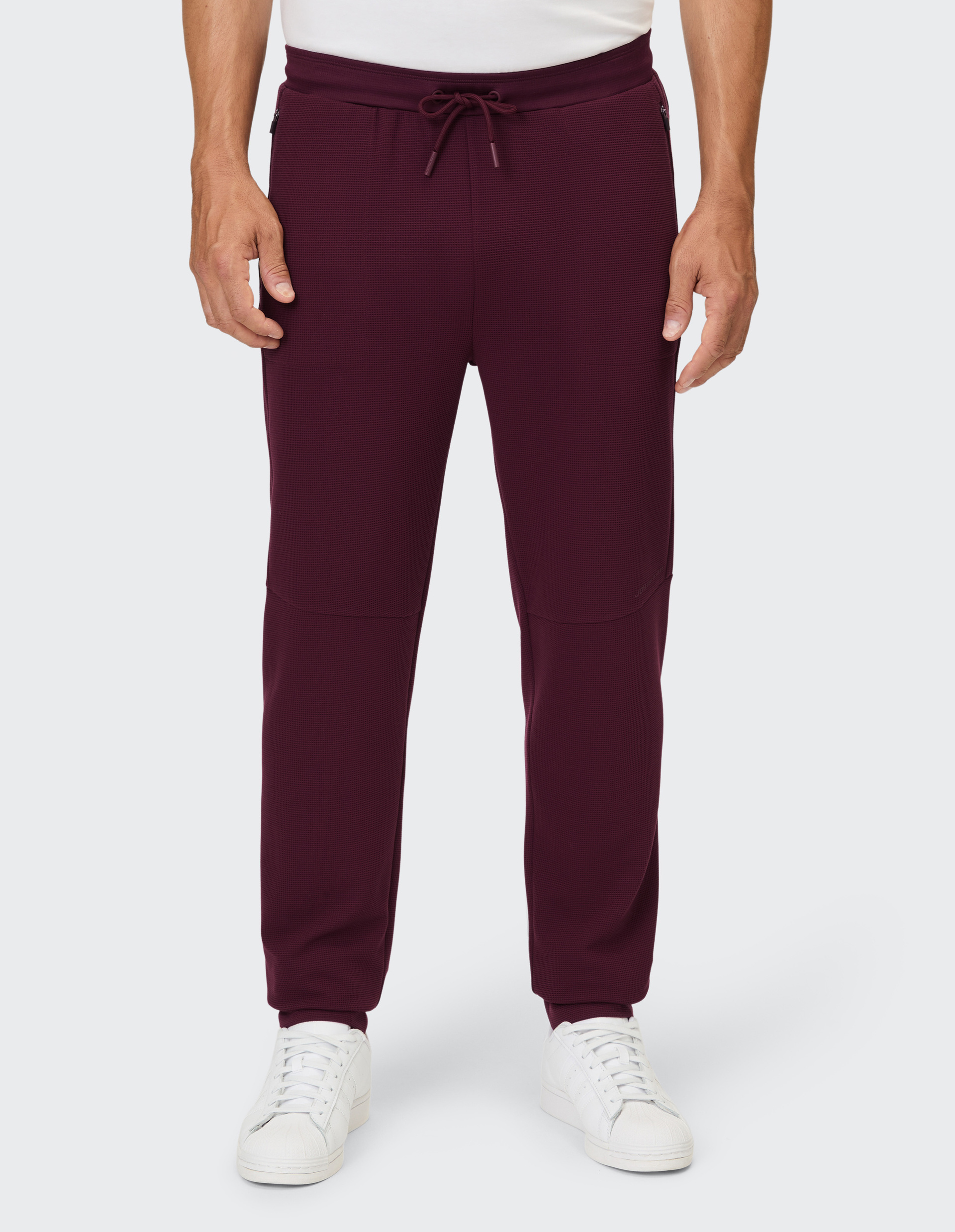 Eine Person trägt eine weinrote Hose mit Waffelmuster, Gummizug und Kordelzug.