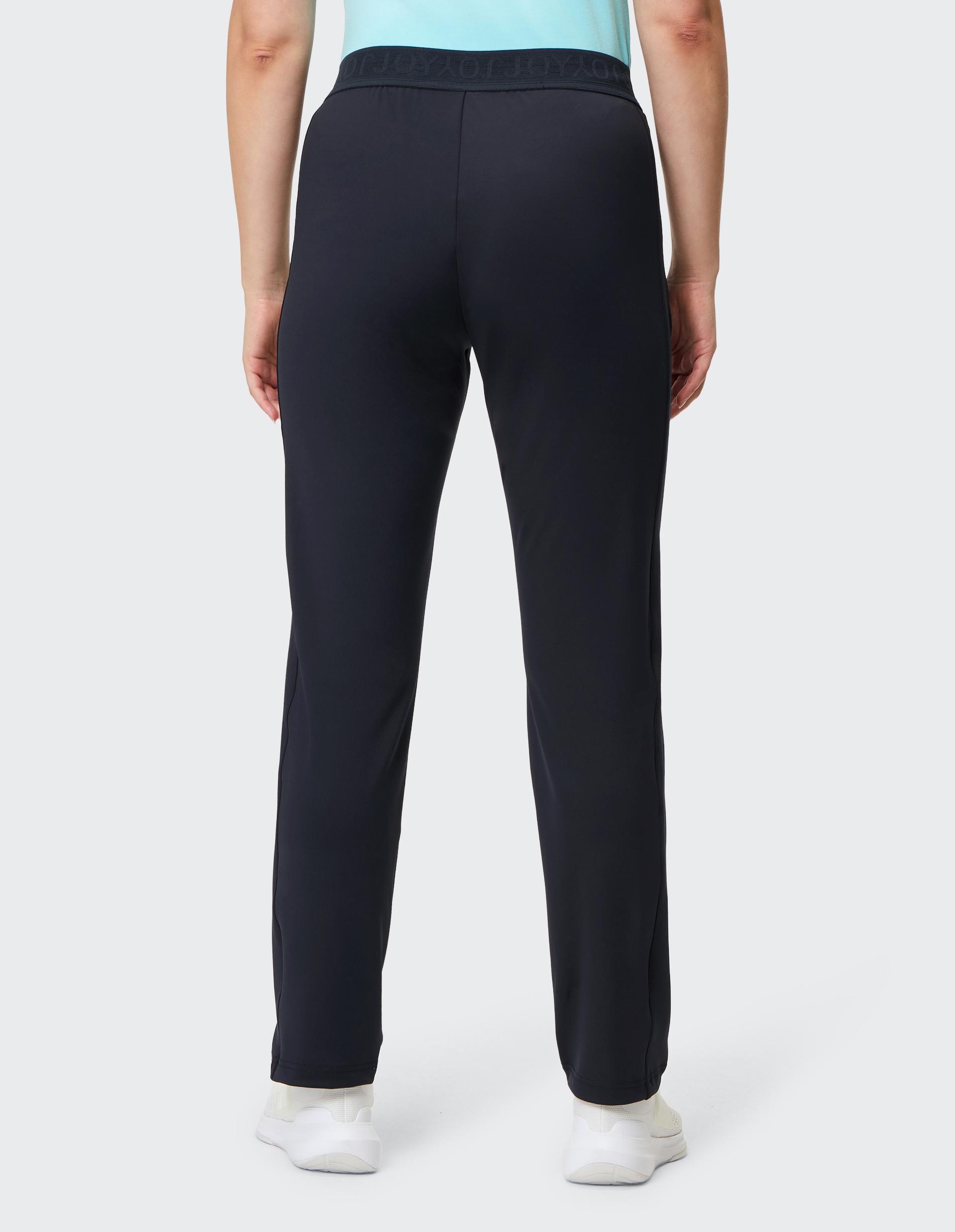 Rückansicht einer Person in schwarzer Trainingshose und türkisfarbenem Oberteil, trägt weiße Sportschuhe auf hellem Hintergrund.