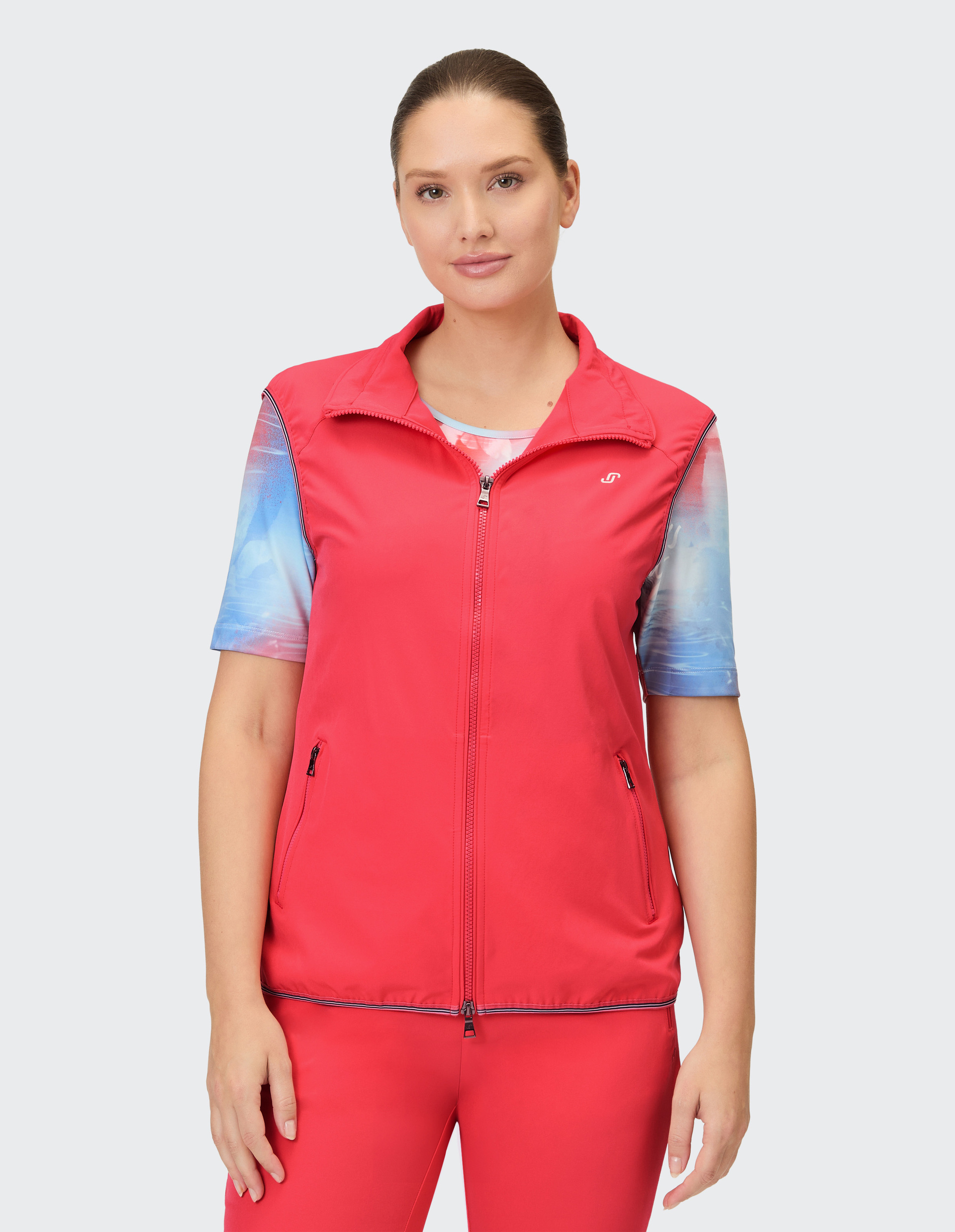 Ein roter Stehkragen-Westen mit Reißverschluss, kombiniert mit einem kurzärmeligen Shirt mit blau-rotem Farbverlauf-Muster.