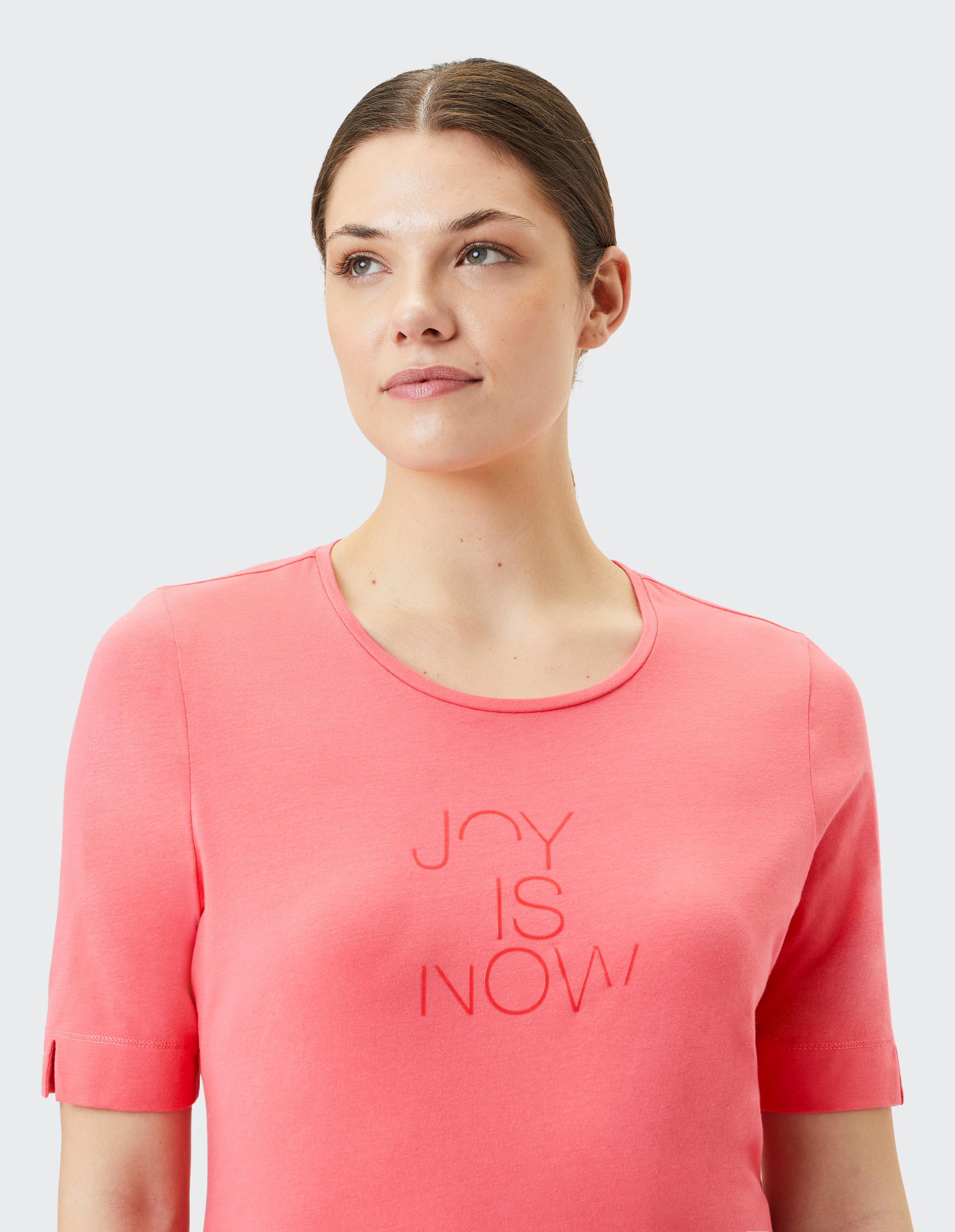 Koralrotes T-Shirt mit rundem Kragen, kurzen Ärmeln und eingeprägtem Schriftzug \\\\\\\"JOY IS NOW\\\\\\\" auf der Vorderseite.
