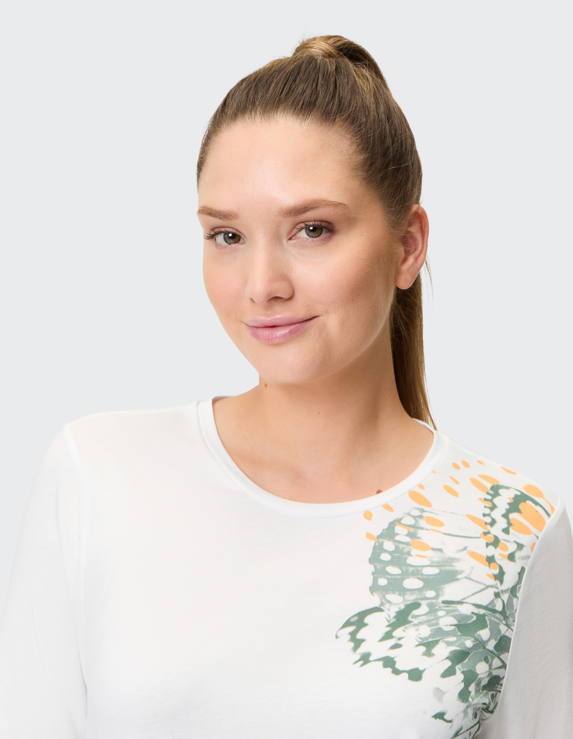 Weißes T-Shirt mit abstraktem Schmetterlingsdruck in Grün und Orange auf Schulter und Vorderseite, Halbärmel, Rundhalsausschnitt.