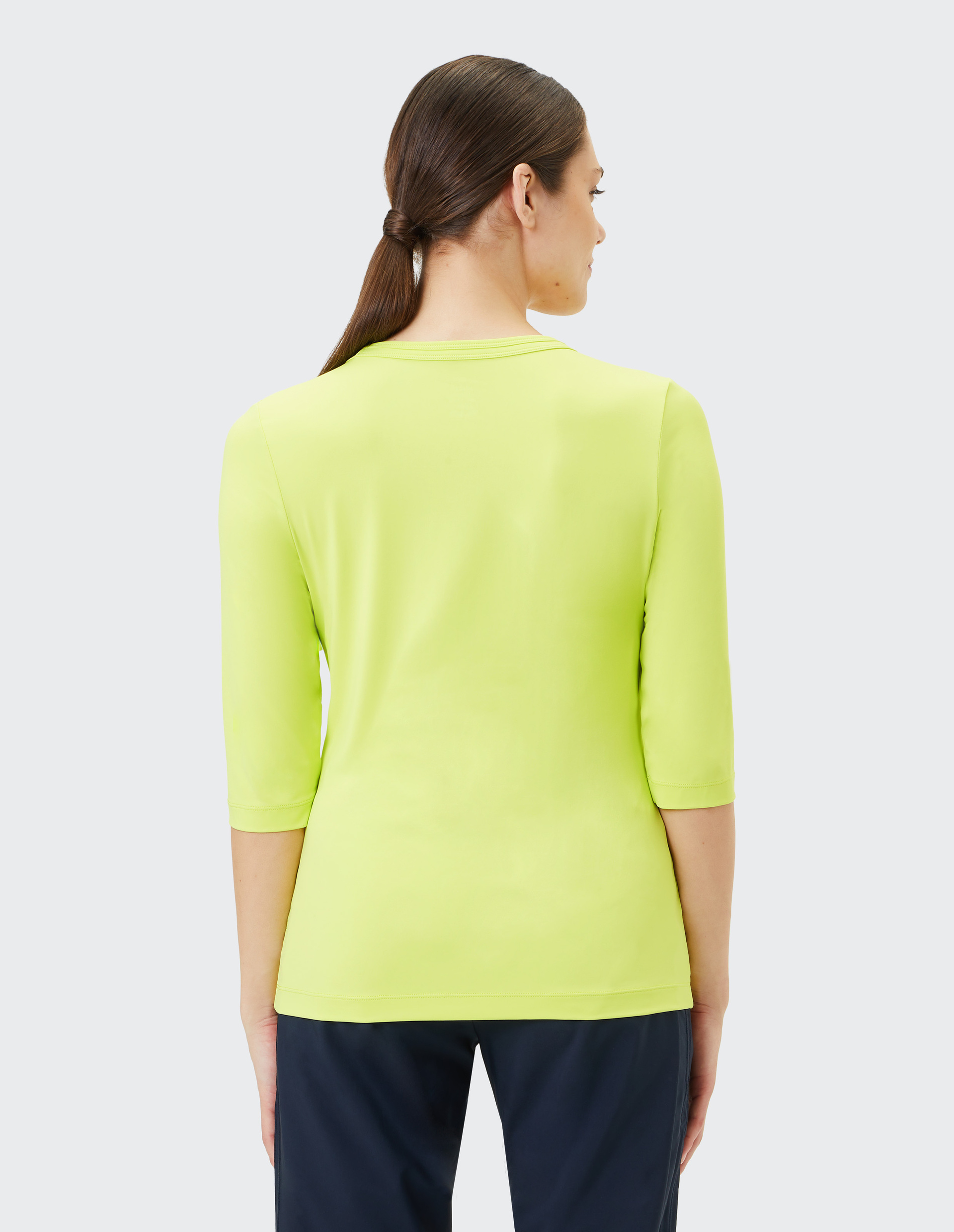 Ein limonengrünes Damen-3/4-Armshirt mit rundem Ausschnitt, schlichtem Design und elastischem Stoff, ideal für sportliche Aktivitäten.