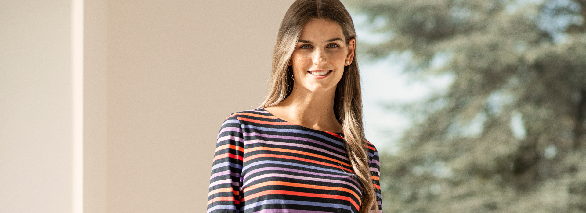 Frau in dunkelblau, hellblau, rot und lila gestreiftem 3/4-Arm-Shirt und dunkelblauer Jogginghose der Marke JOY sportswear.