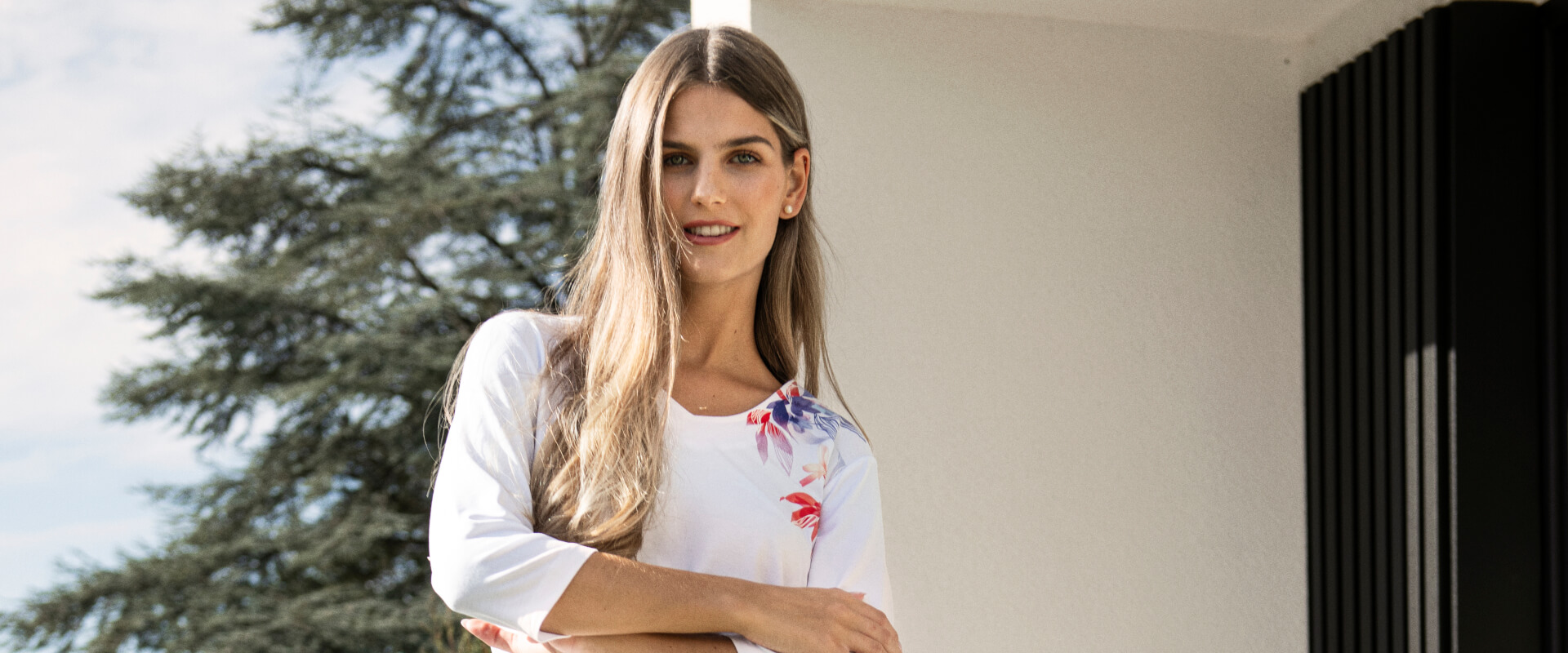 Frau in weißem Shirt mit floralen Details und blauer Jogginghose auf Terrasse