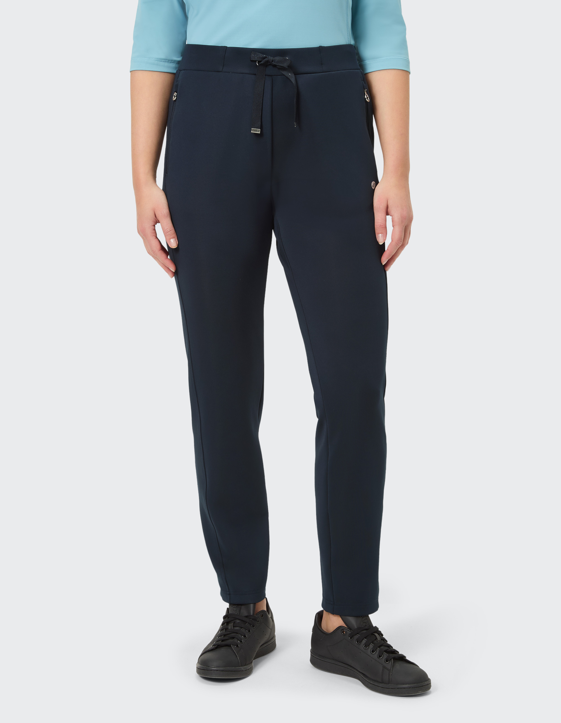 Person trägt eine dunkelblaue Hose mit Tunnelzug und schwarzen Sneakers, kombiniert mit einem hellblauen Oberteil auf hellem Hintergrund.