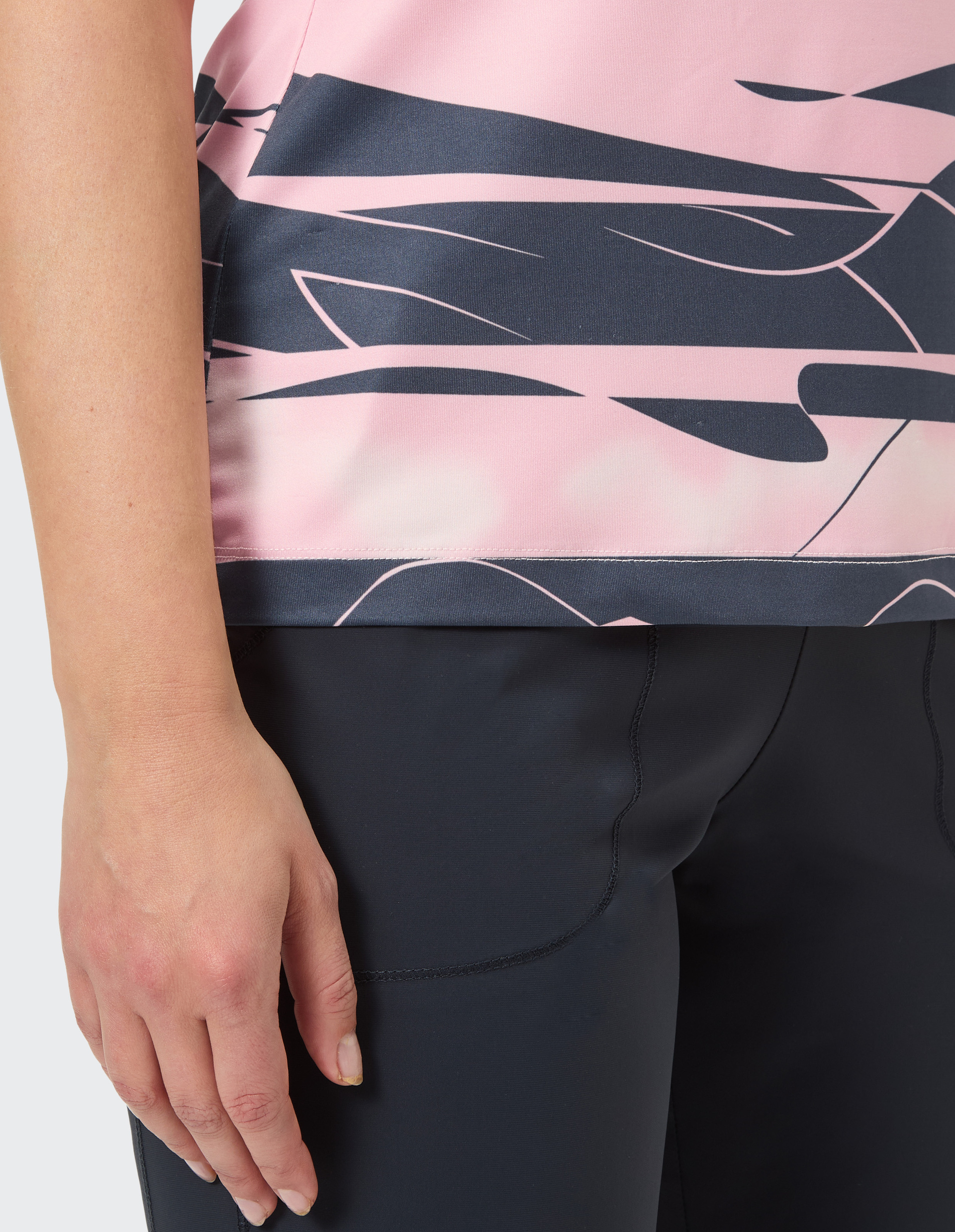 Nahaufnahme einer Hand neben einem pink-schwarz gemusterten Oberteil und einer dunkelblauen Hose vor grauem Hintergund.