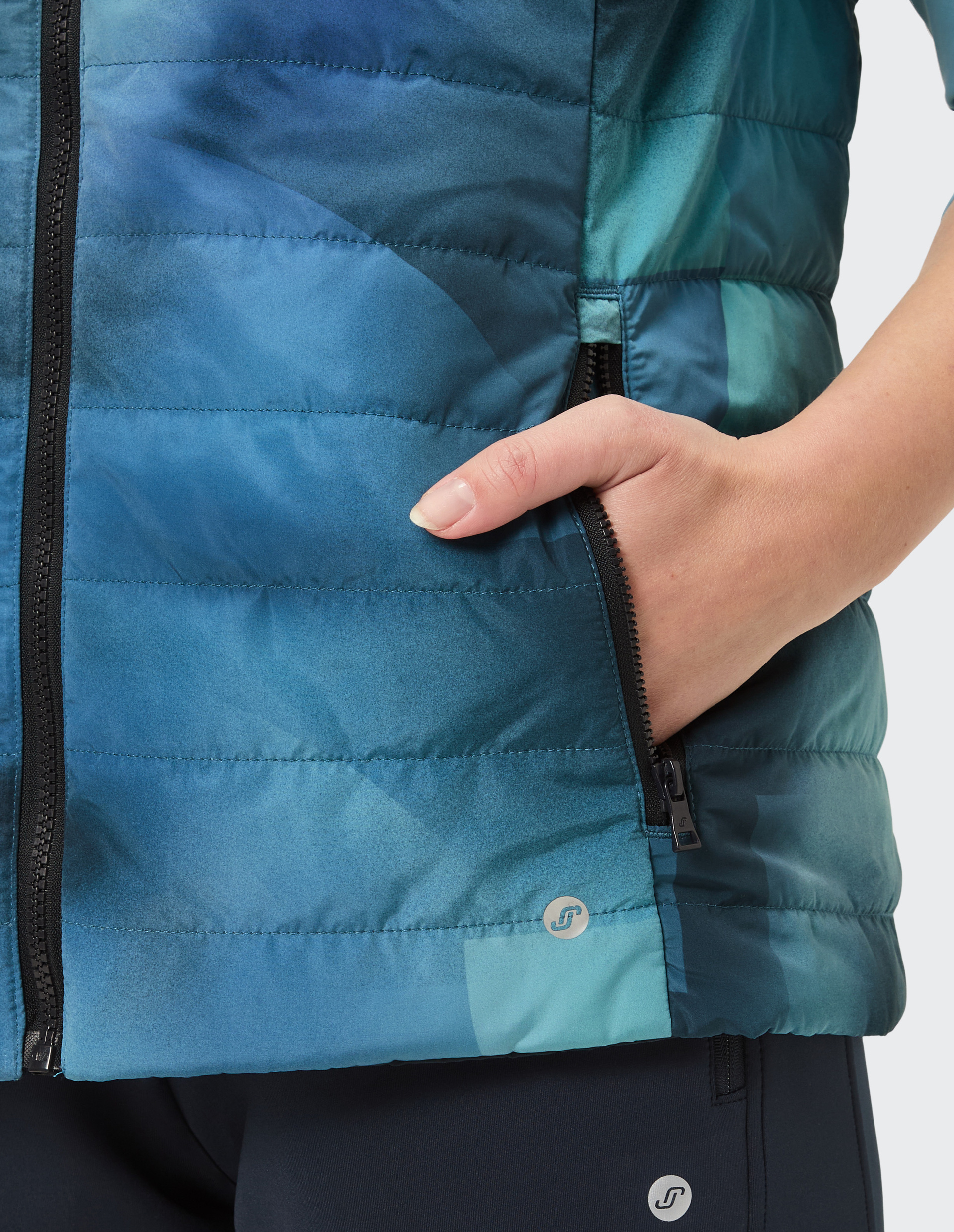 Hand steckt in der Tasche einer blau gemusterten Steppjacke mit Reißverschluss, Detailaufnahme des Designs.