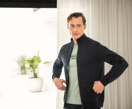 Mann in dunkelblauer Sweatjacke und mintfarbenem T-Shirt der Marke JOY sportswear.