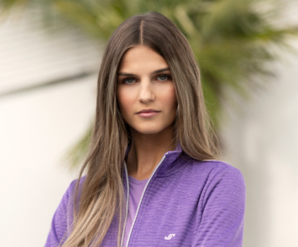 Frau in lila-melierter Sweatjacke und lilafarbenem T-Shirt der Marke JOY sportswear.