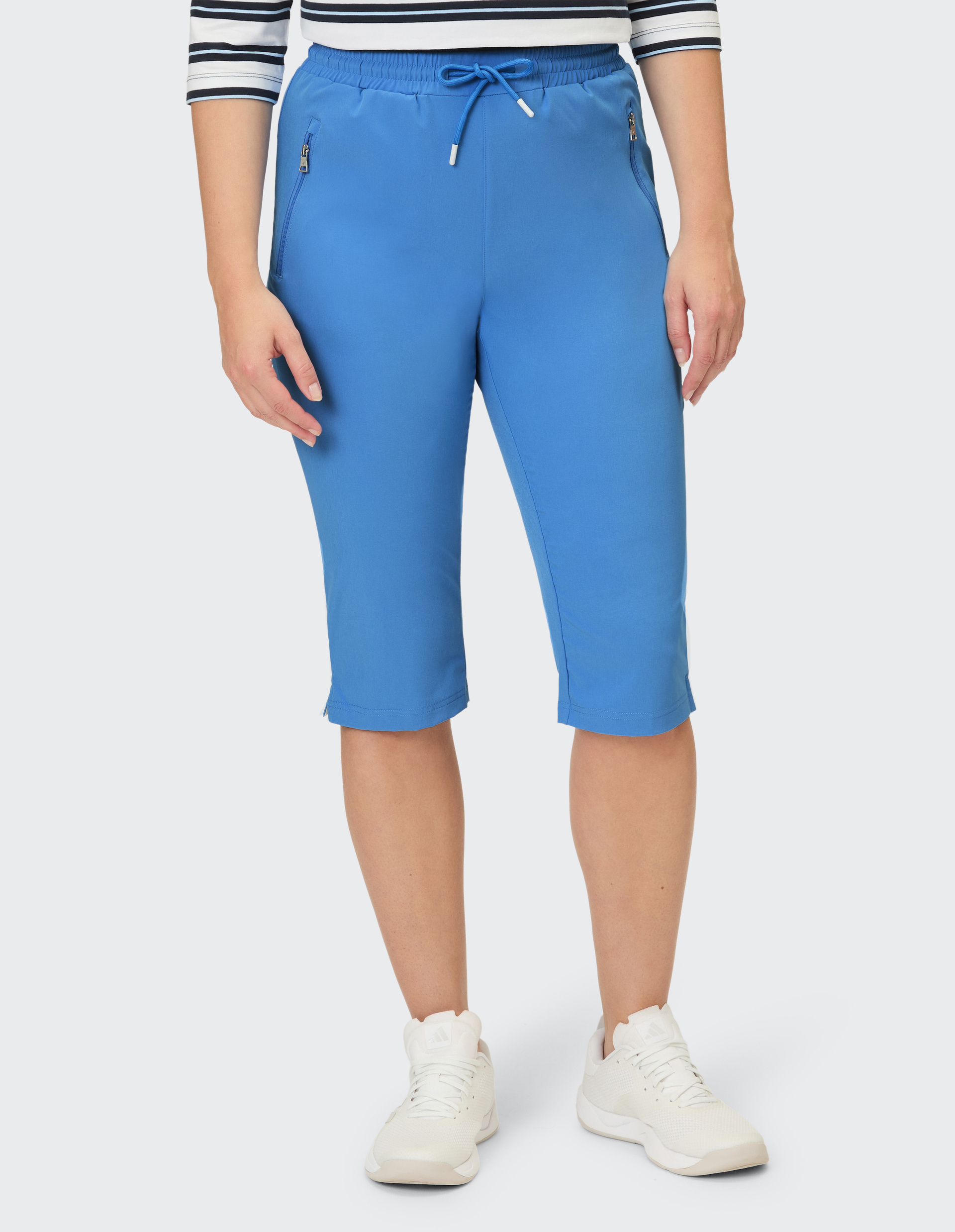 Blaue Capris mit Kordelzug und Reißverschlusstaschen, getragen von einer Person mit gestreiftem Oberteil und weißen Turnschuhen.