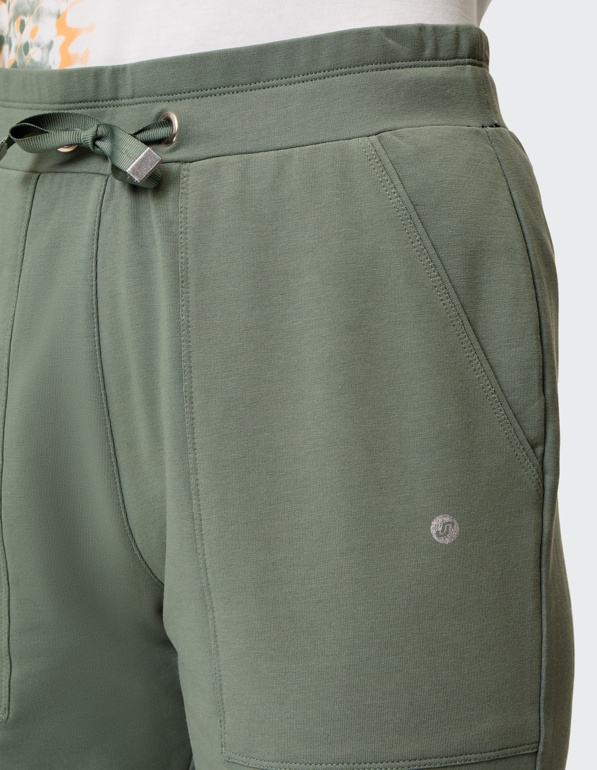 Grüne Shorts mit Kordelzug, Seitentaschen und dezentem Logo, getragen mit einem weißen T-Shirt mit farbigem Muster.