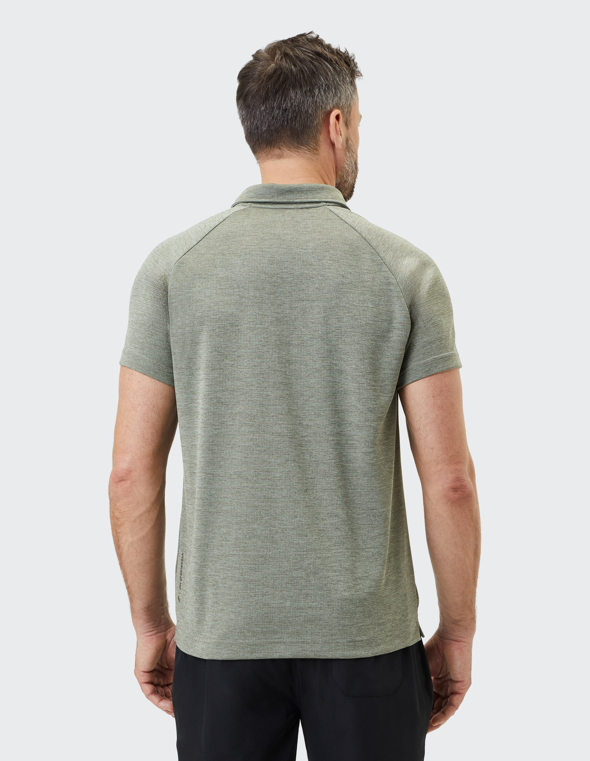 Ein Mann in einem graugrünen Poloshirt steht mit dem Rücken zur Kamera, seine kurzen Haare sind dunkel und der Hintergrund ist neutral.