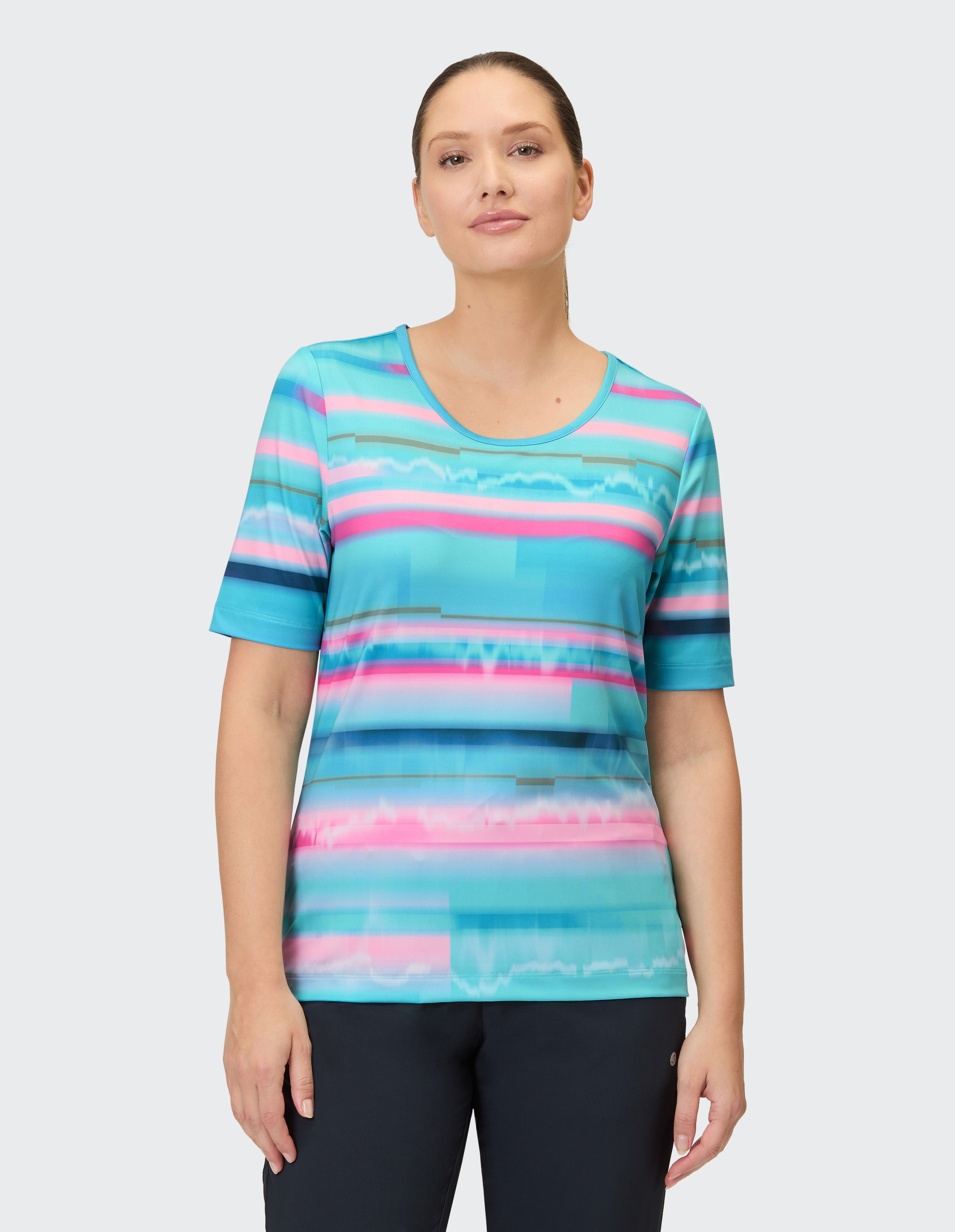 Eine Frau trägt ein kurzärmeliges Shirt mit Streifen in Blau-, Rosa- und Grautönen, das sich wie ein abstraktes Farbmuster über das gesamte Kleidungsstück zieht.