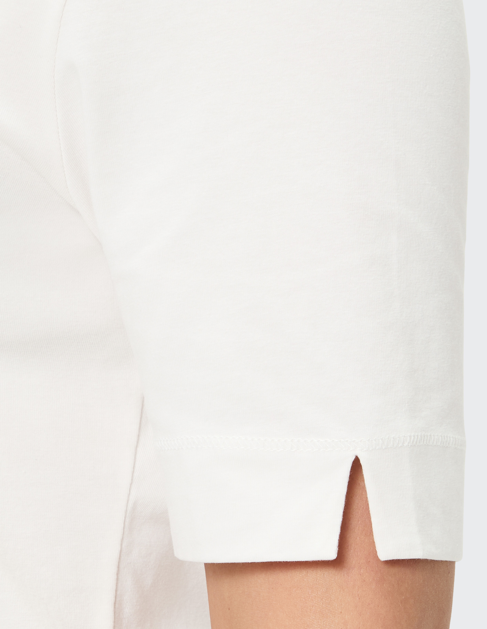 Detailaufnahme eines weißen T-Shirts mit kurzen Ärmeln, die einen kleinen seitlichen Schlitz haben, nahe der Schulternaht.