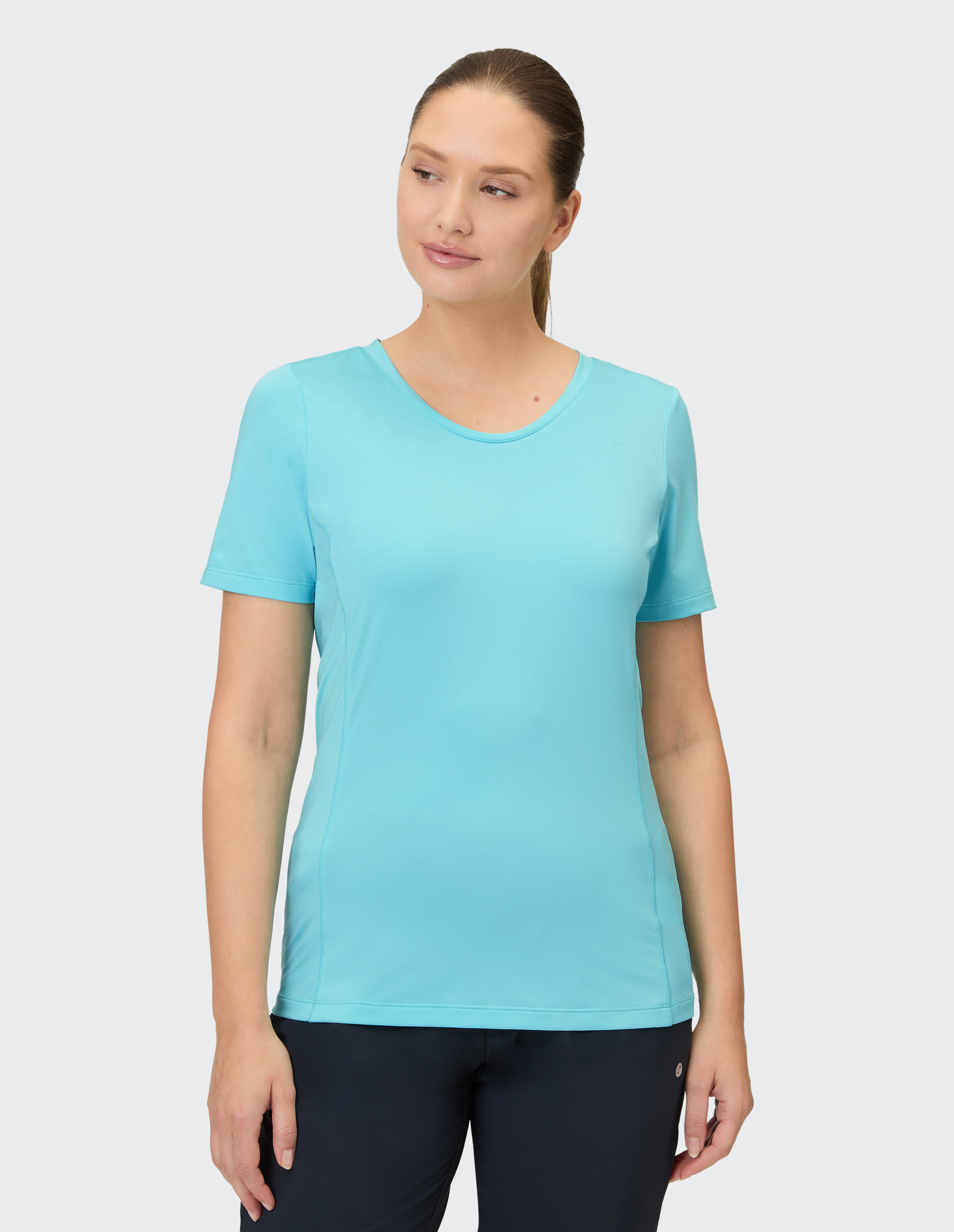 Eine Frau trägt ein hellblaues T-Shirt mit kurzen Ärmeln und eine dunkle Hose.