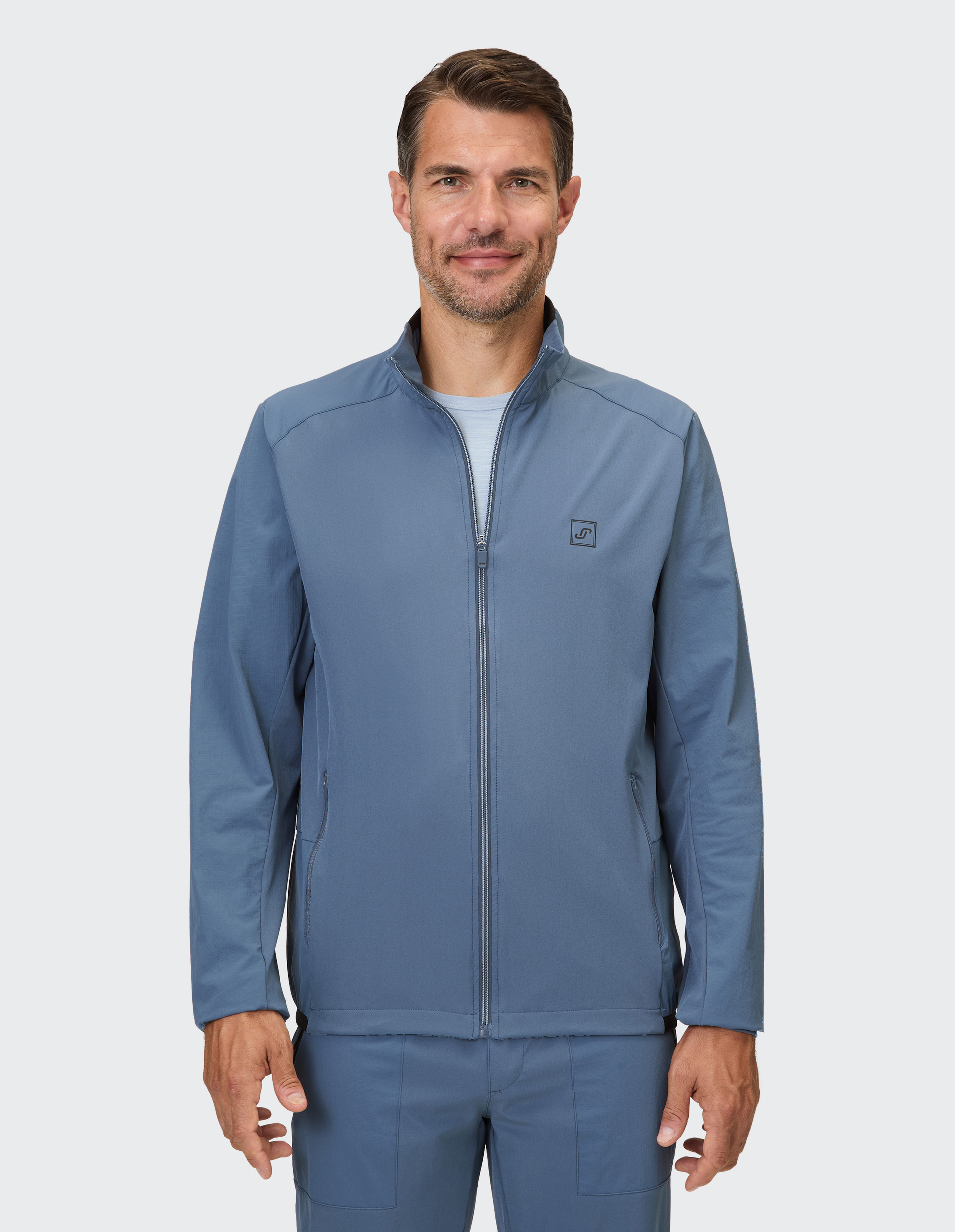 Ein Mann trägt eine marineblaue Reißverschlussjacke mit Stehkragen und einer aufgestickten Logoplatte am linken Ärmel.