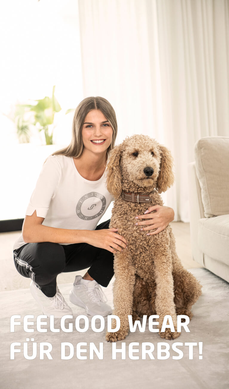 Junge Frau hockt lächelnd neben einem beigefarbenen Pudel mit Halsband und trägt helle Ober- und dunkle Unterbekleidung.