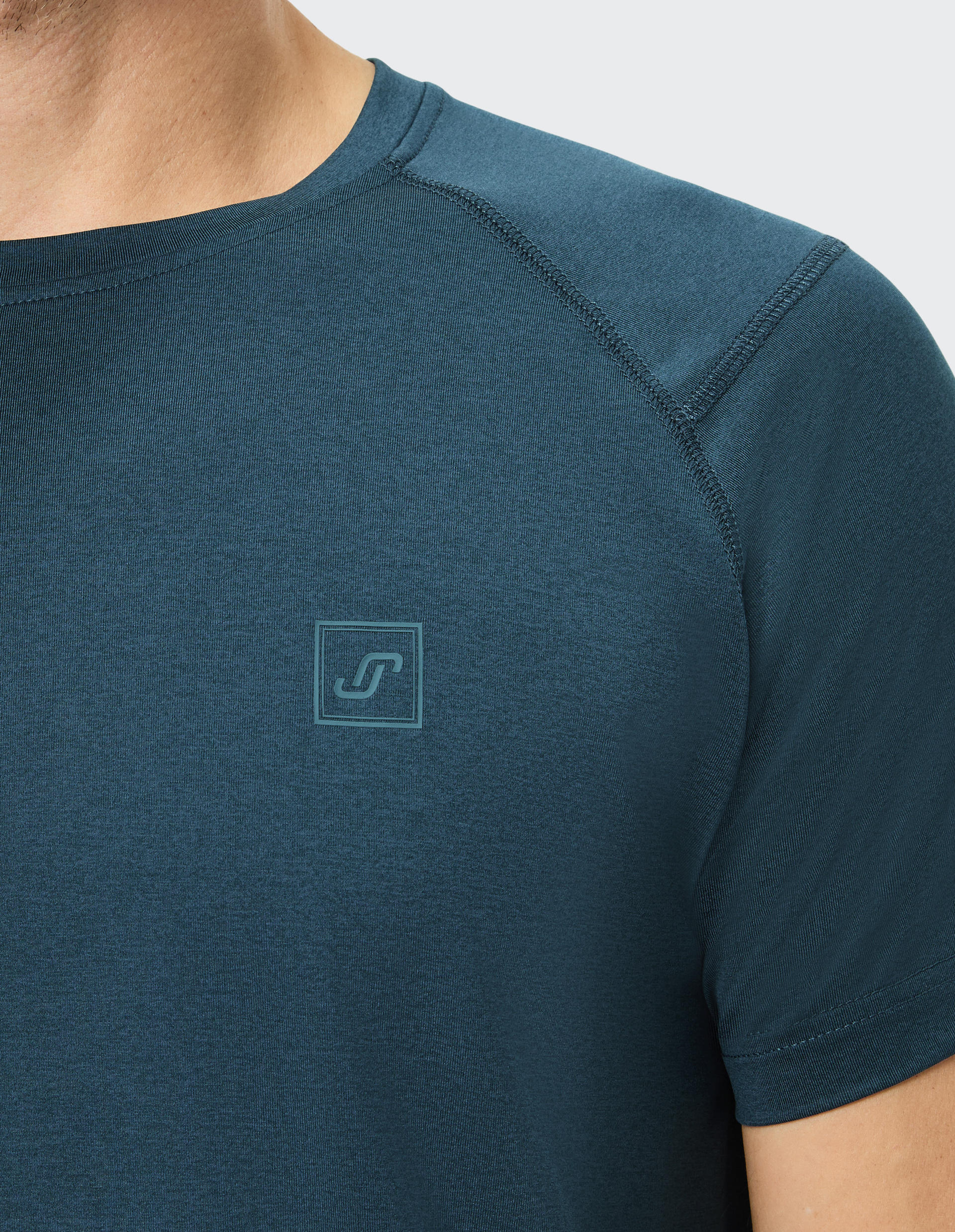 Nahaufnahme eines dunkelblauen T-Shirts mit rundem Halsausschnitt und kleinem Logo-Emblem auf der Brust, getragen von einer Person.