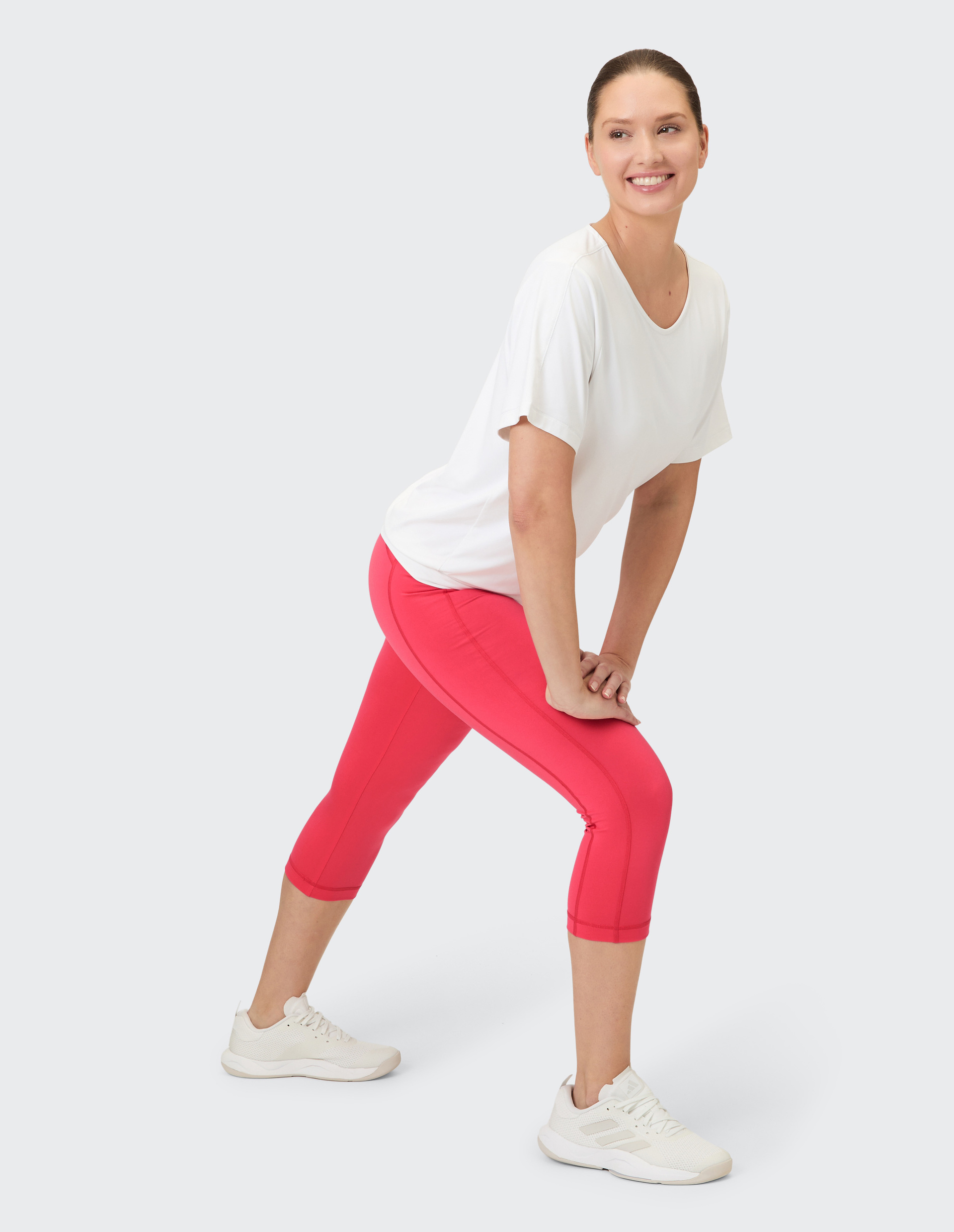 Eine Frau in einem weißen T-Shirt und roten 3/4-Hosen macht eine Dehnung.
