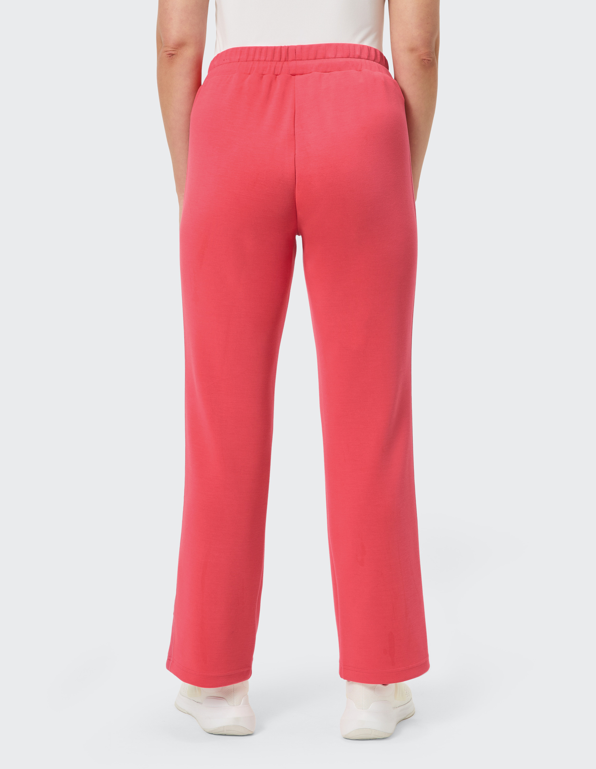 Person in roten, locker geschnittenen Jogginghosen und weißen Sneakern von hinten, stehend auf hellem Hintergrund.