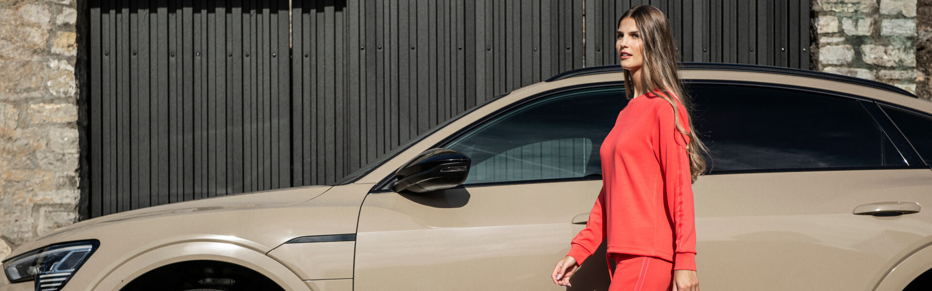 Frau in rotem Anzug der Marke JOY sportswear läuft vor beigem Auto.