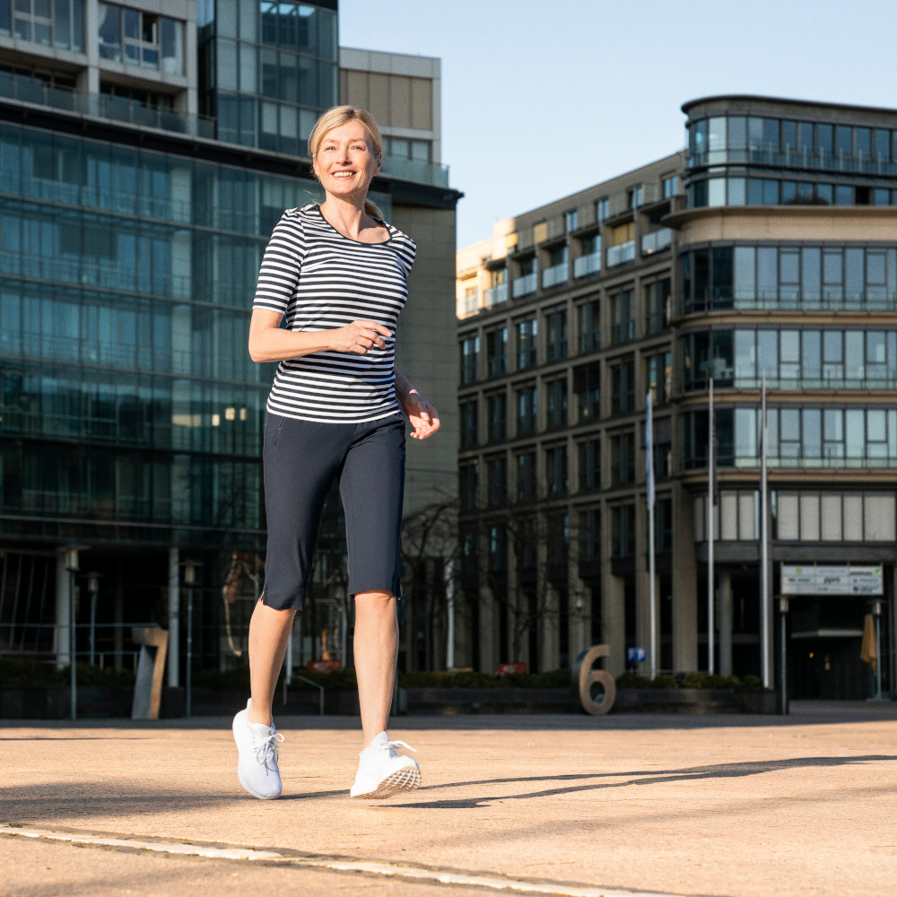 Frau joggt in Sportklamotten der Marke JOY sportswear vor zwei Gebäuden.