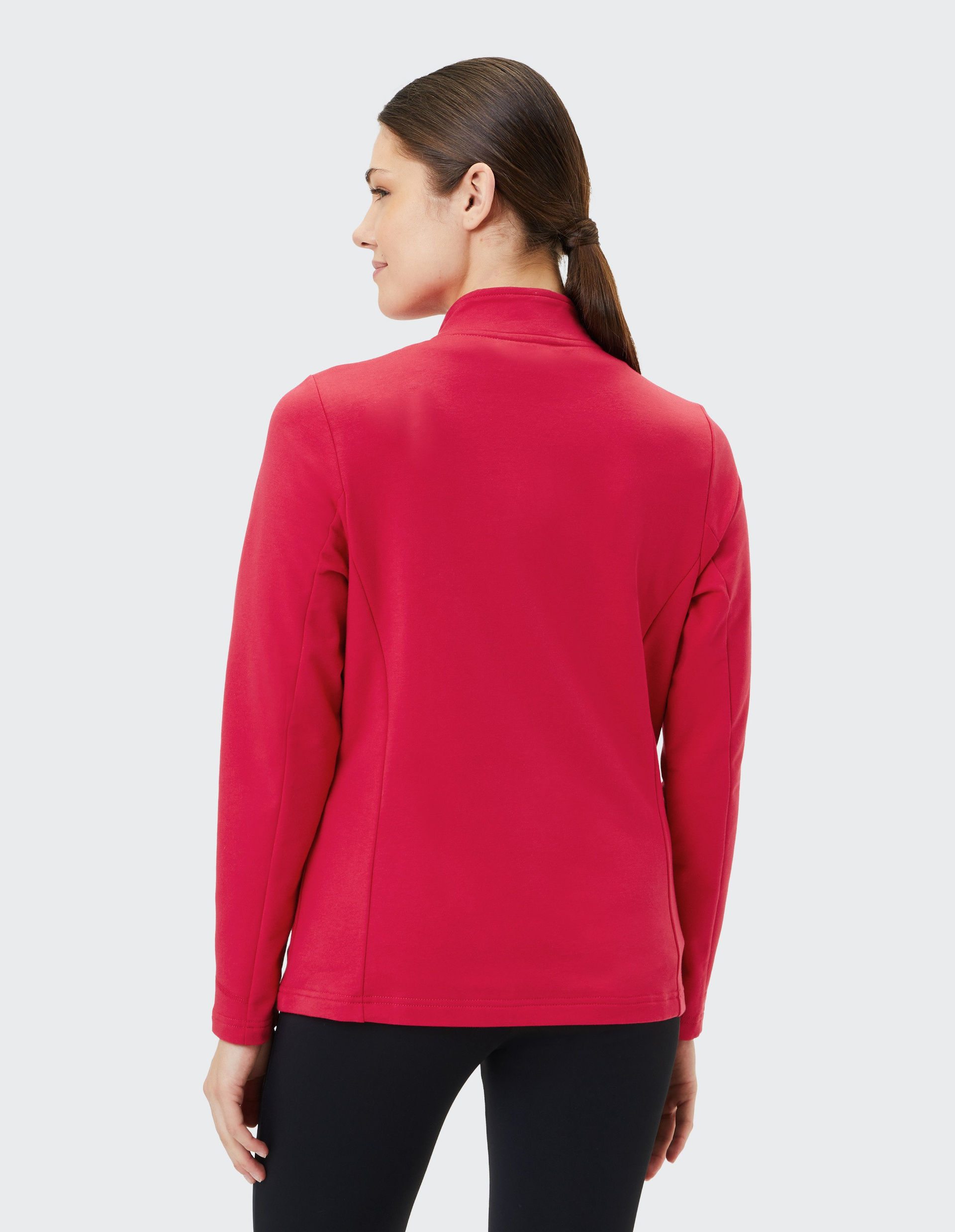 Frau mit glattem, dunklem Haar in Pferdeschwanz trägt eine rote Jacke und blickt zur Seite, vor hellem Hintergrund.