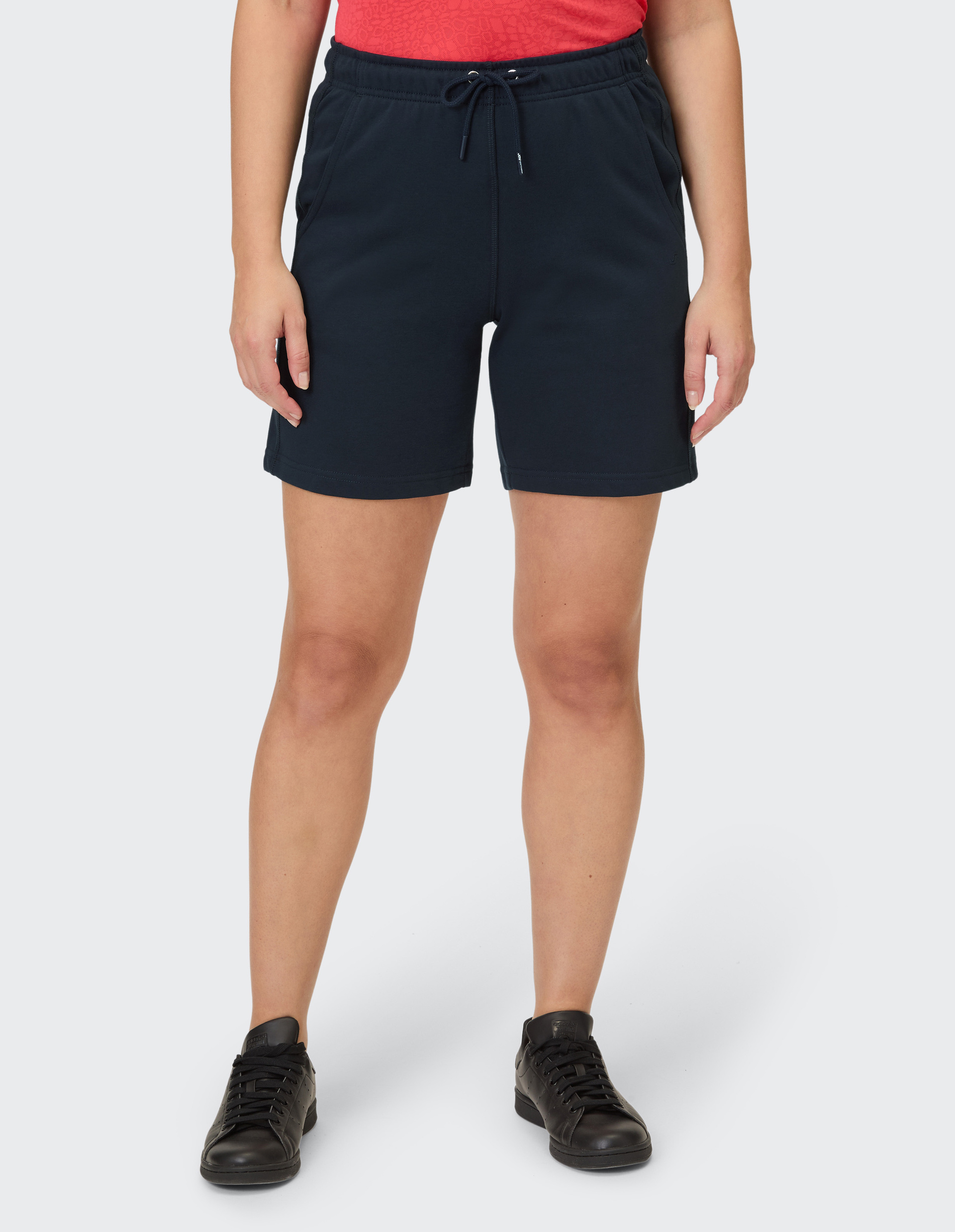 Eine Person trägt dunkelblaue Shorts mit Kordelzug und ein rotes Oberteil mit Muster.