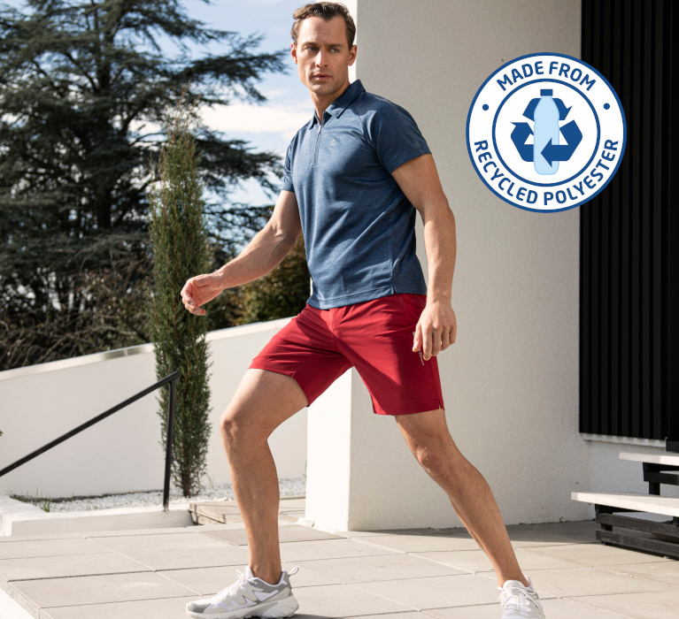 Mann in dunkelblau-meliertem Zip-Poloshirt und roter Shorts der Marke JOY sportswear in sportlicher Pose. In der Ecke des Bildes ist das Zeichen für Recycled Polyester angebracht.