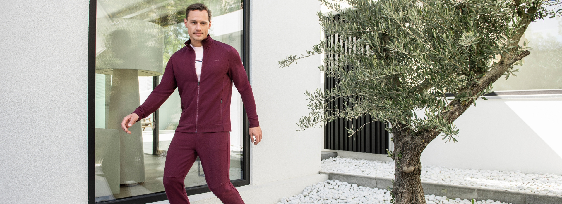 Mann in rotem Anzug in sportlicher Pose auf einer Terrasse.