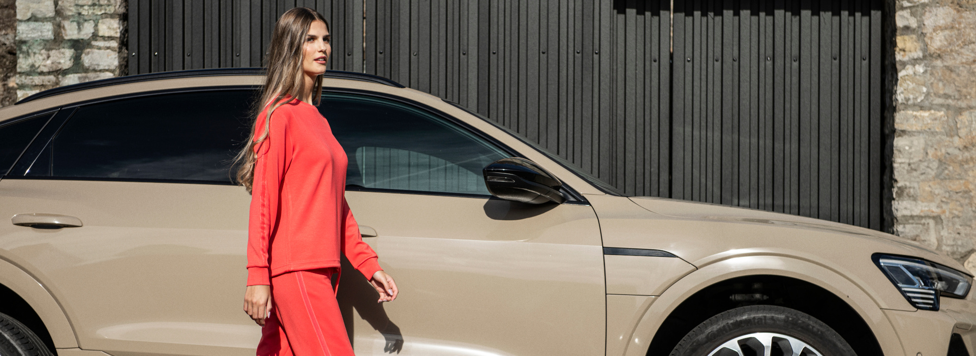 Frau läuft in roten Oberteil und gleichfarbiger Hose der Marke JOY sportswear vor einem Auto.