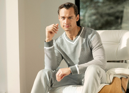 Mann mit grauem Sweatshirt und Hose der Marke JOY sportswear sitzt auf einem weißen Sessel.