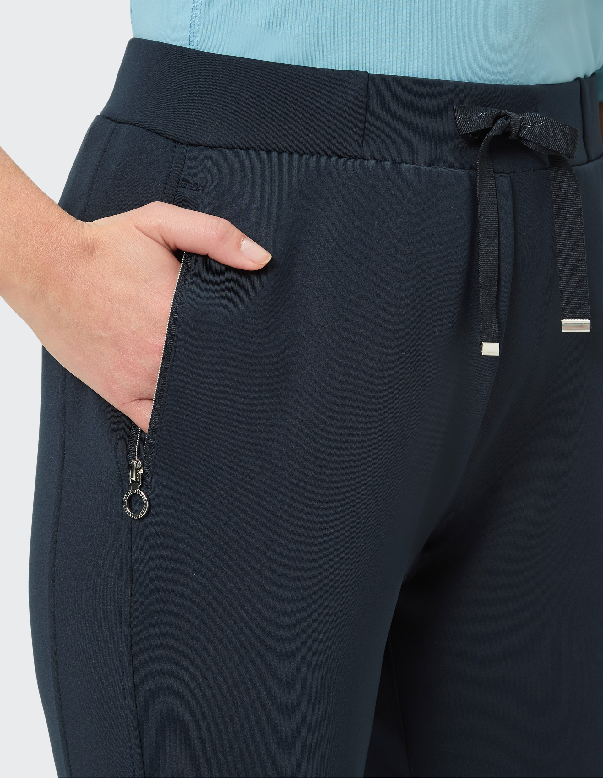 Dunkelblaue Hose mit seitlichem Reißverschluss, Schleifenbändern und einer Hand, die lässig in der Tasche steckt.