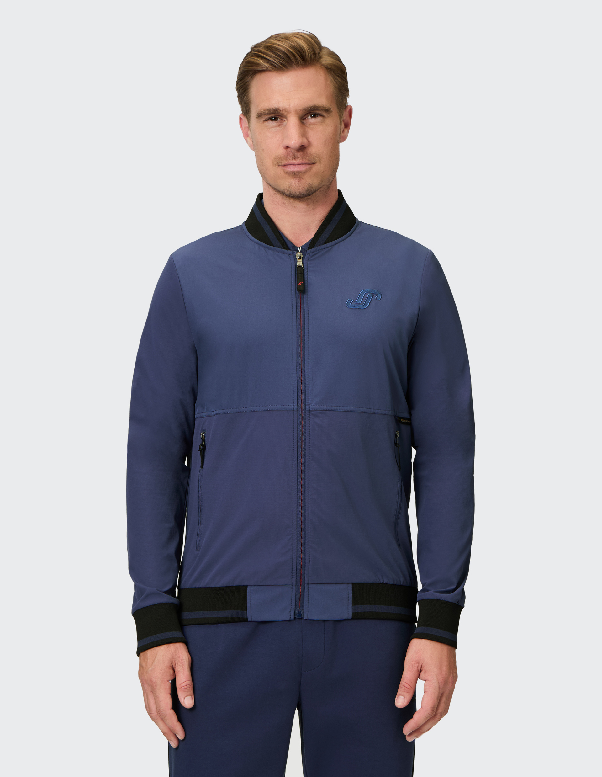 Dunkelblaue Bomberjacke mit schwarzem Kragen, Reißverschluss, gesticktem Logo links, und seitlichen Reißverschlusstaschen.
