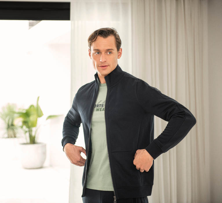 Mann in dunkelblauer Sweatjacke und mintfarbenem T-Shirt der Marke JOY sportswear.