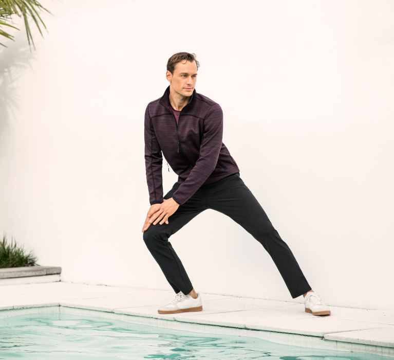 Mann in roter Sweatjacke und dunkler Hose der Marke JOY sportswear in sportlicher Pose.
