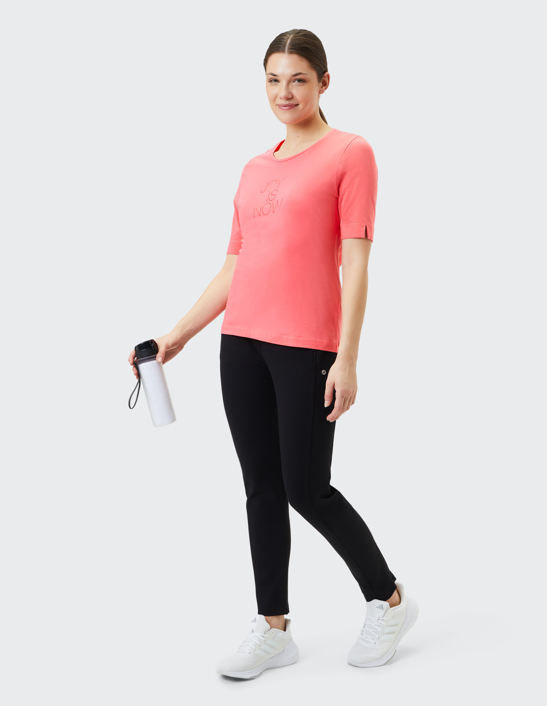 Koralrotes T-Shirt mit rundem Kragen, kurzen Ärmeln und eingeprägtem Schriftzug "JOY IS NOW" auf der Vorderseite.