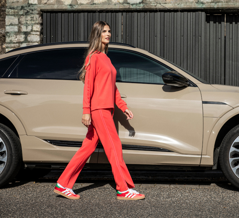 Frau läuft in roten Oberteil und gleichfarbiger Hose der Marke JOY sportswear vor einem Auto.