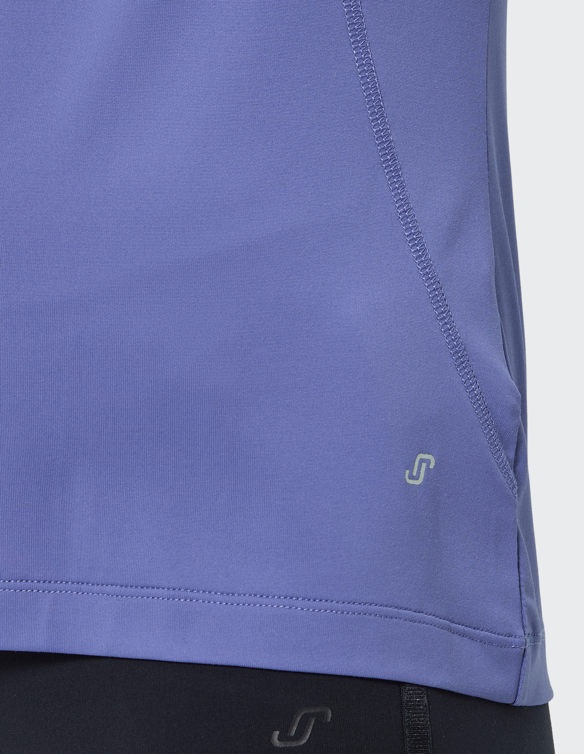 Detailaufnahme eines lilafarbenen Sportshirts mit dezentem Logo auf der Hüfte und kontrastierenden Nähten neben einem schwarzen Stoff.