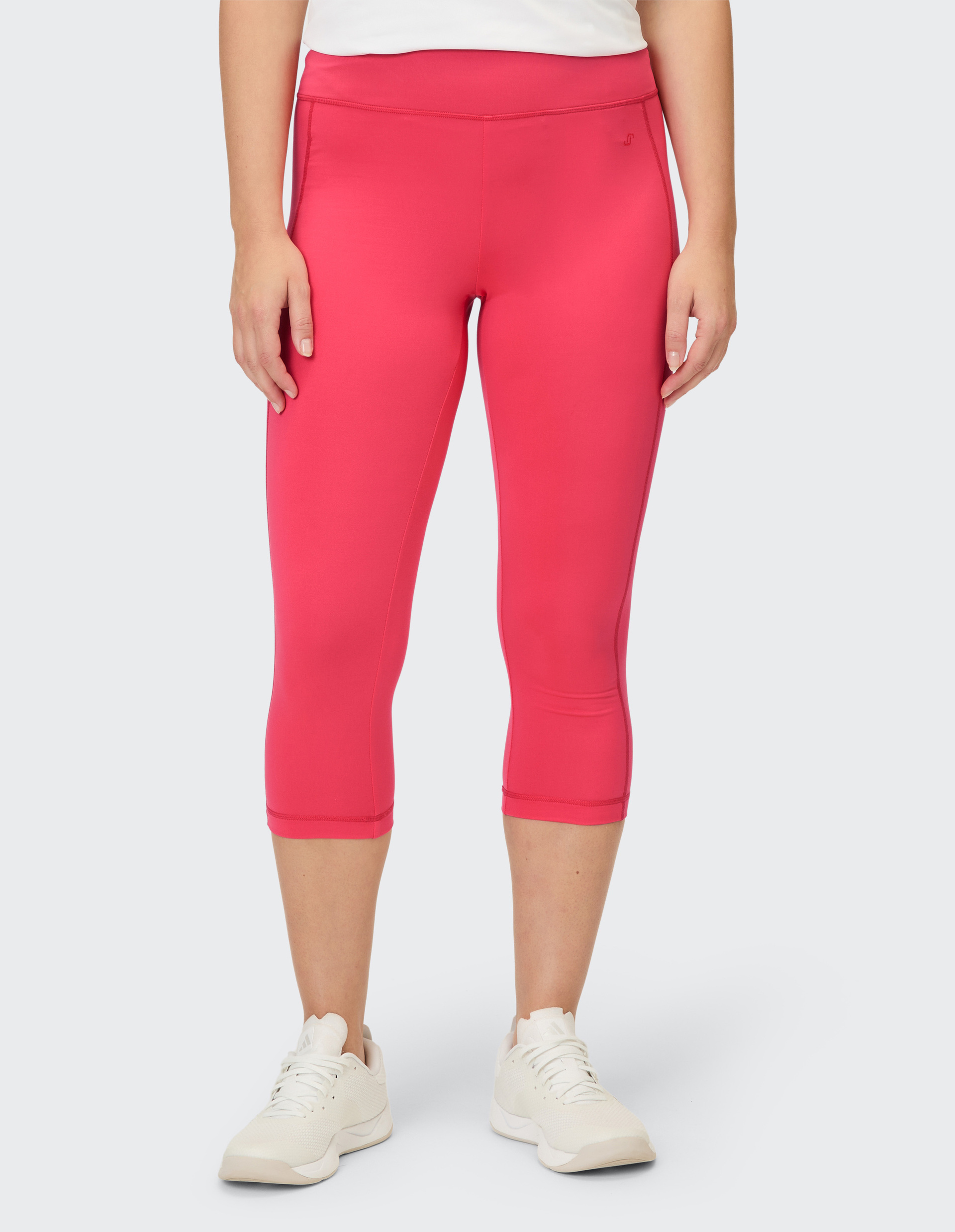 Eine Person trägt knielange, leuchtend pinke Leggings und weiße Sportschuhe.