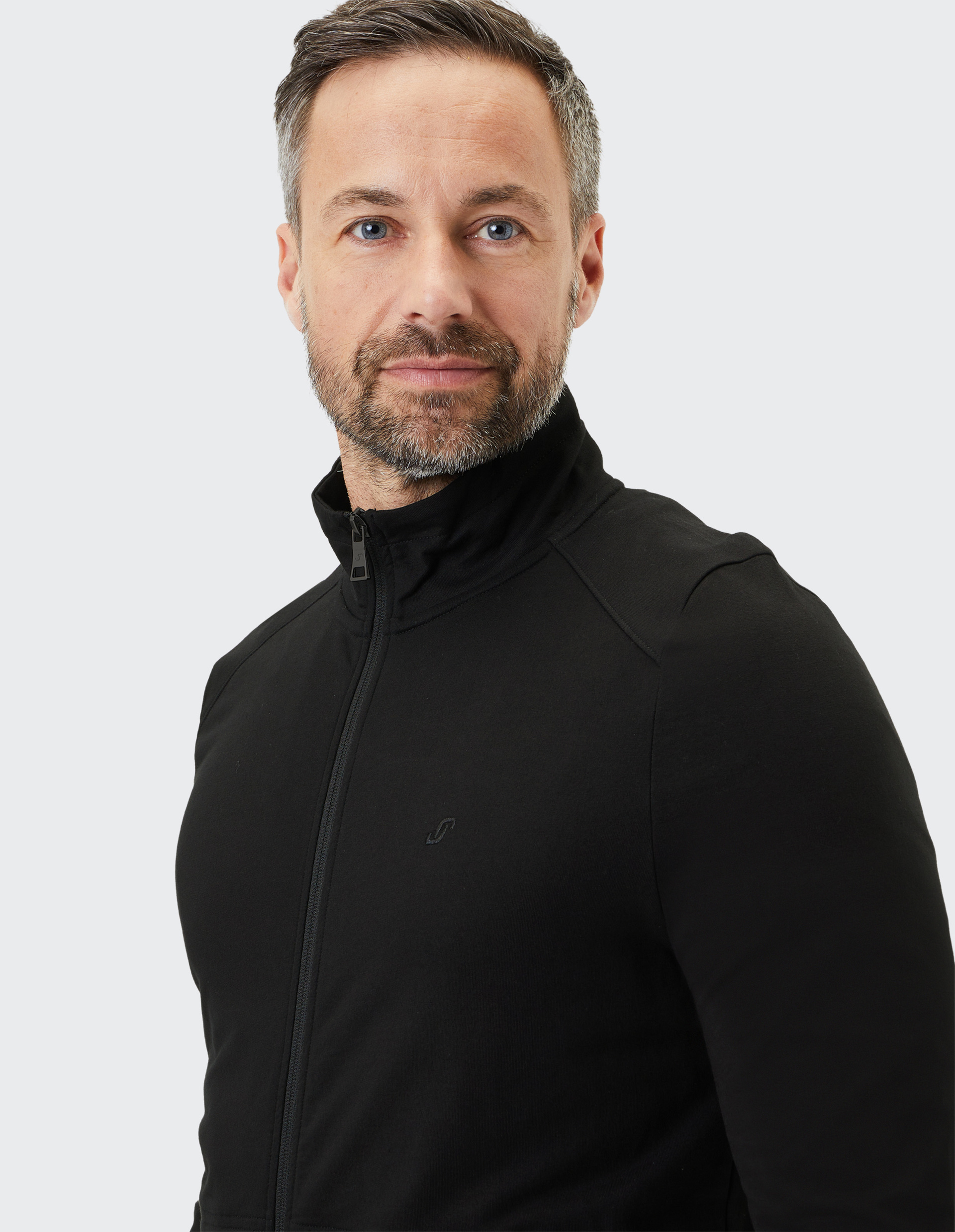 Ein Mann mit Bart, grauem Haar und schwarzem Rollkragenpullover blickt freundlich in die Kamera, vor grauem Hintergrund.