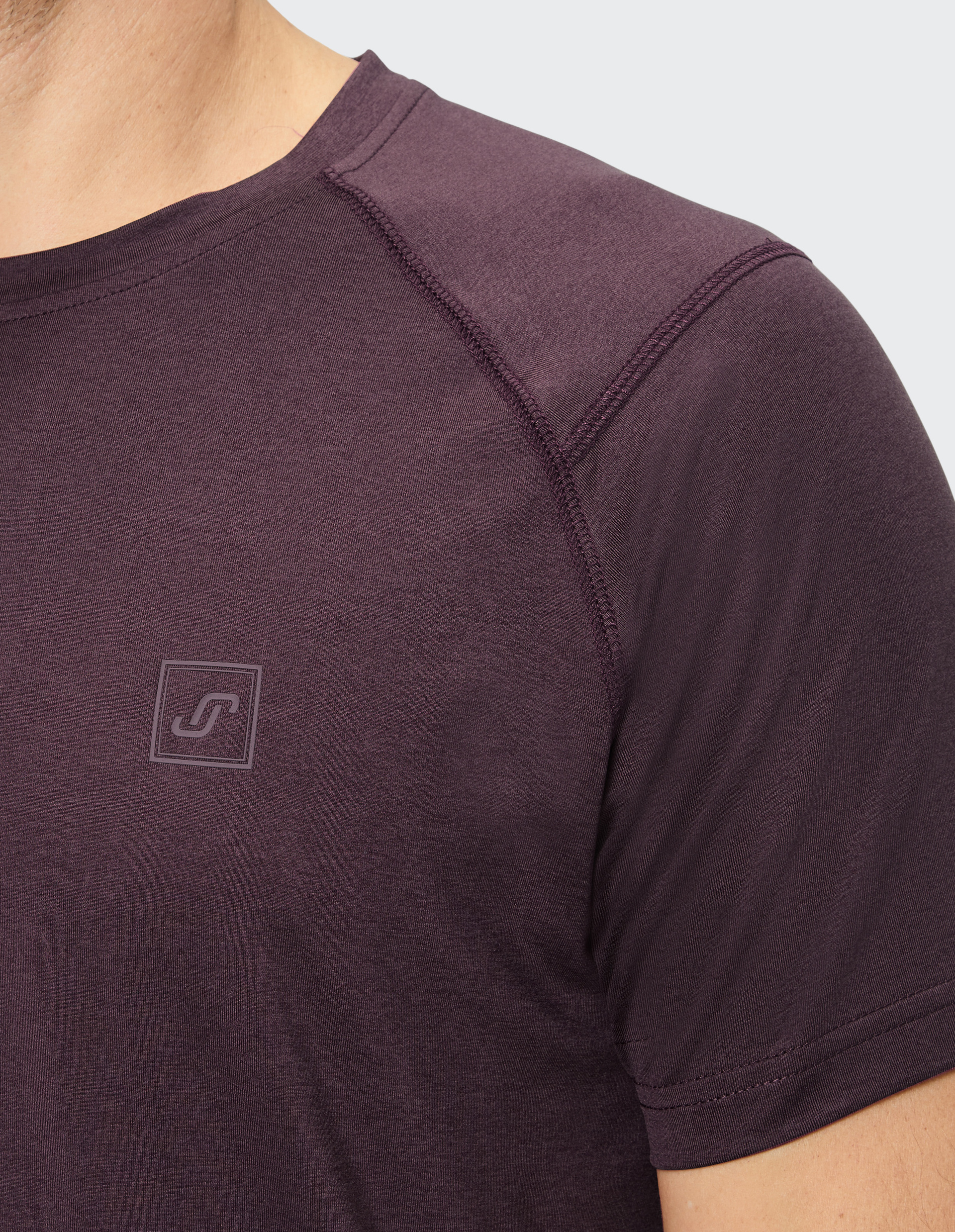 Nahaufnahme eines Mannes in einem dunkelvioletten T-Shirt mit kurzen Ärmeln und dezenter Naht; Logo auf der Brust.