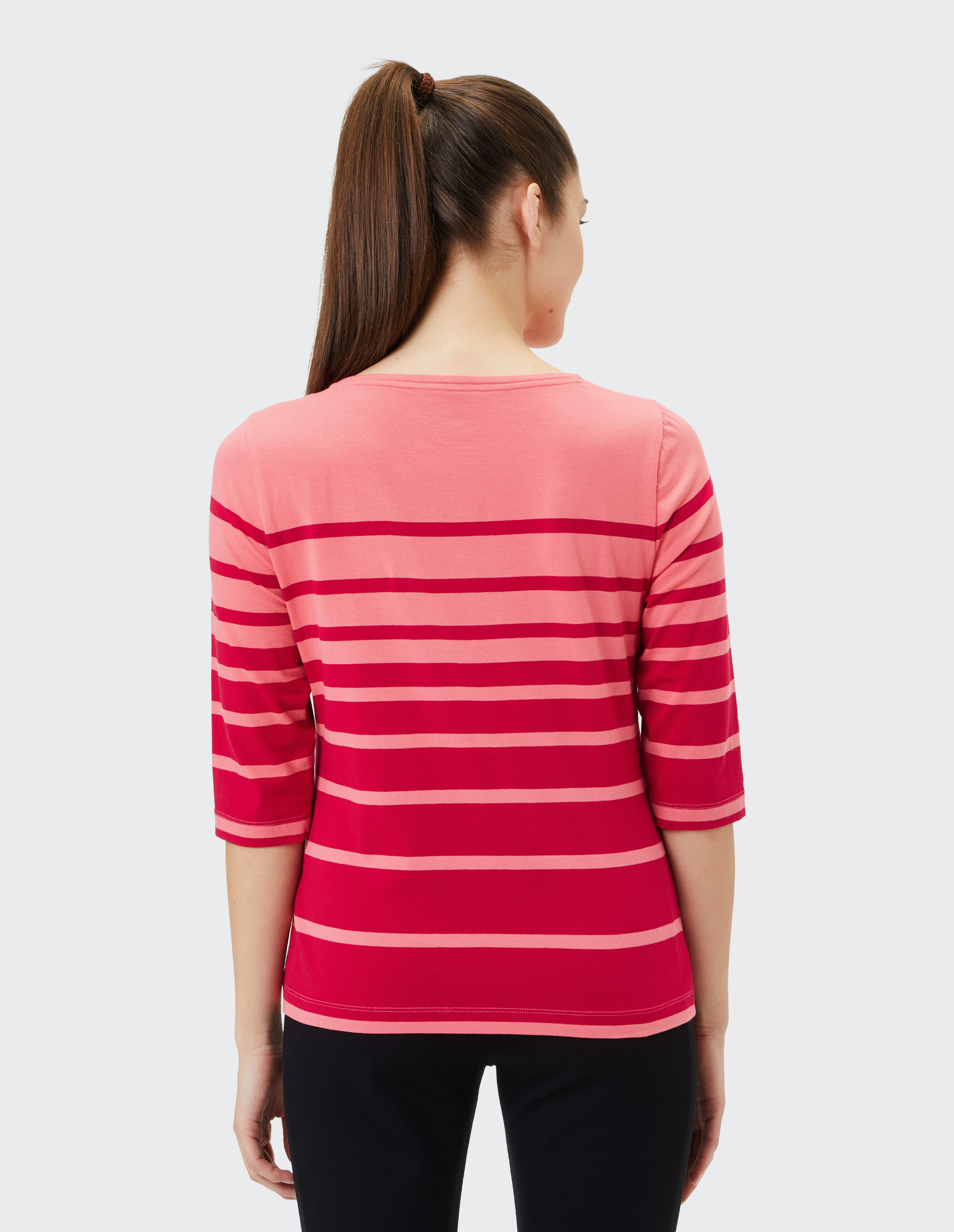 Frau von hinten in rosa-rot gestreiftem Shirt mit Dreiviertelärmeln, dunkelhaarig mit Pferdeschwanz, trägt schwarze Hose.
