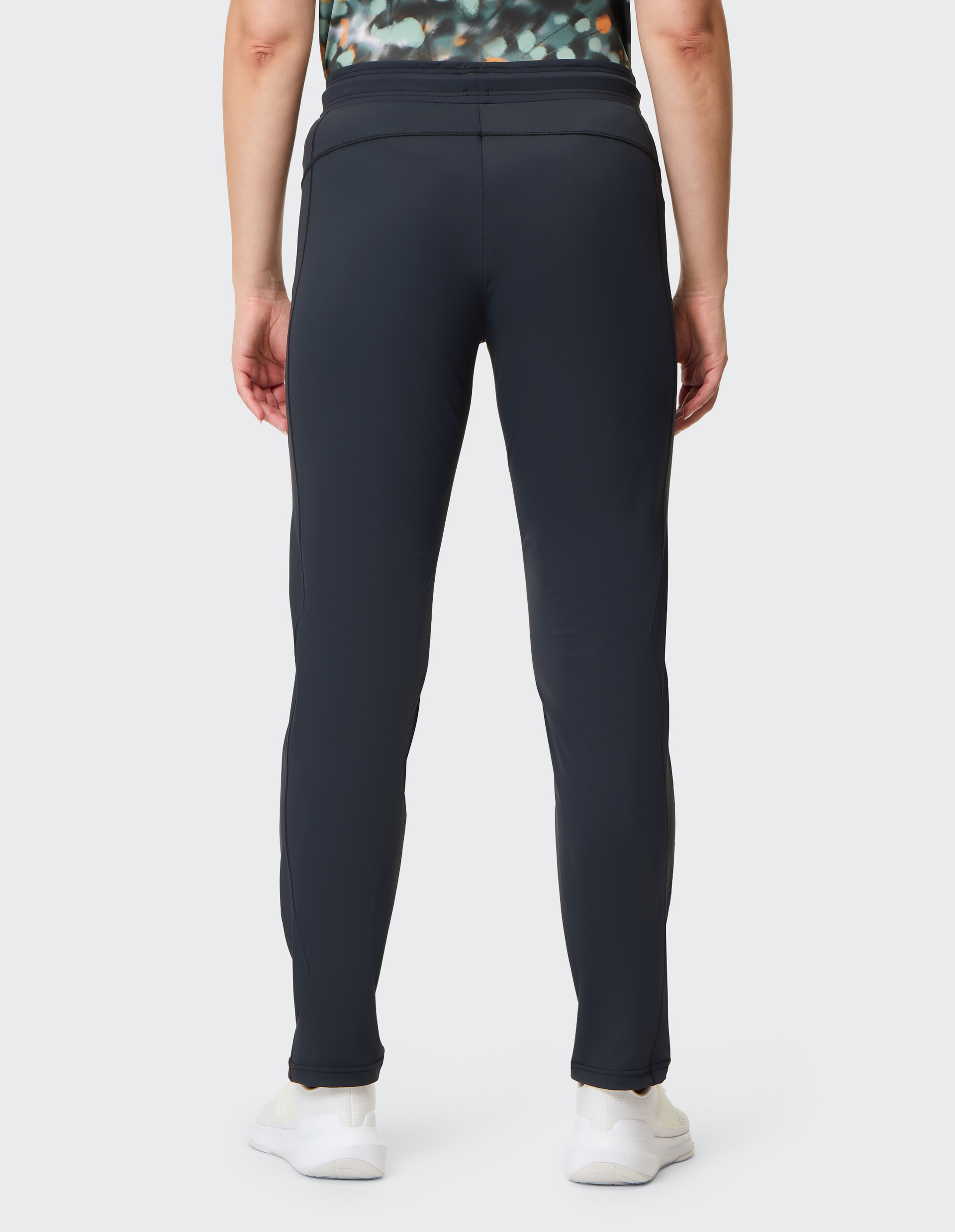 Person trägt schwarze Sporthose und weiße Schuhe, von hinten fotografiert, mit einem Oberteil in gemusterten Farben.