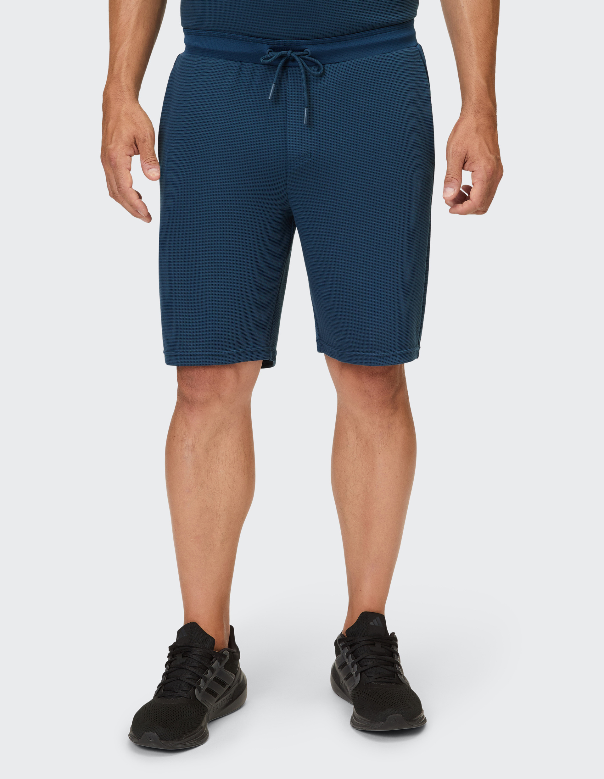 Dunkelblaue Shorts mit Waffelmuster und Kordelzug, getragen über schwarzen Turnschuhen.
