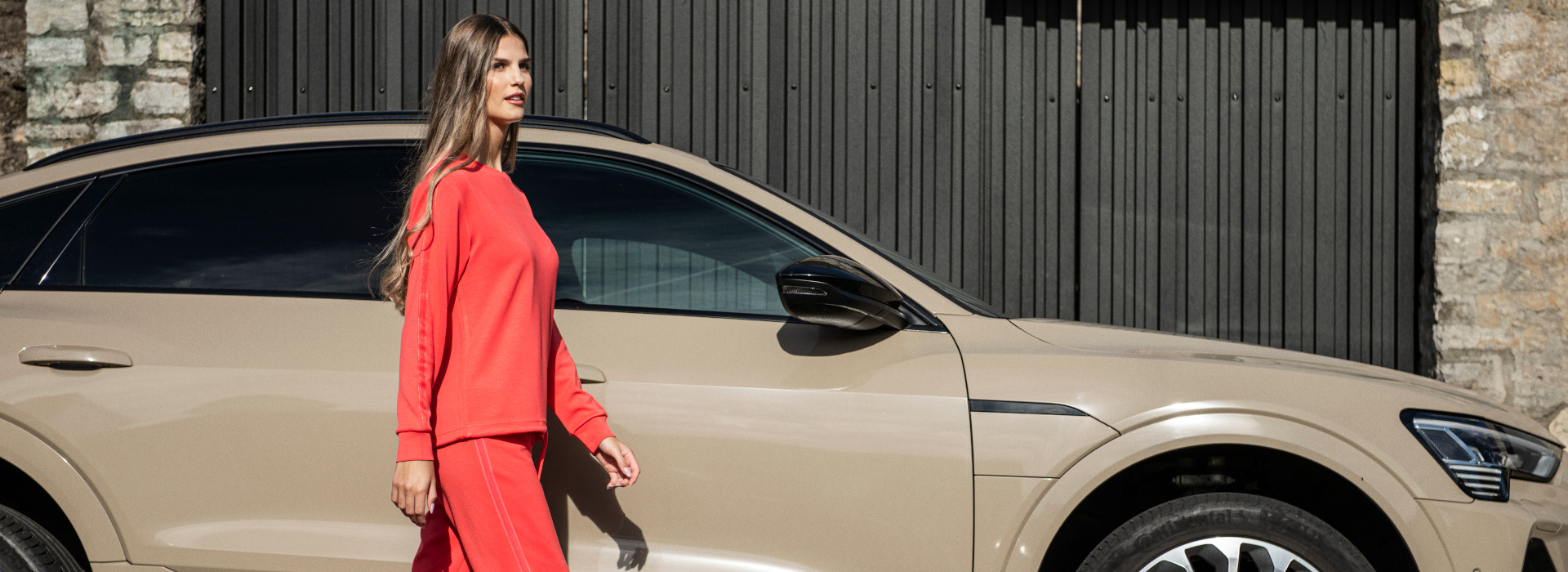 Frau läuft in roten Oberteil und gleichfarbiger Hose der Marke JOY sportswear vor einem Auto.