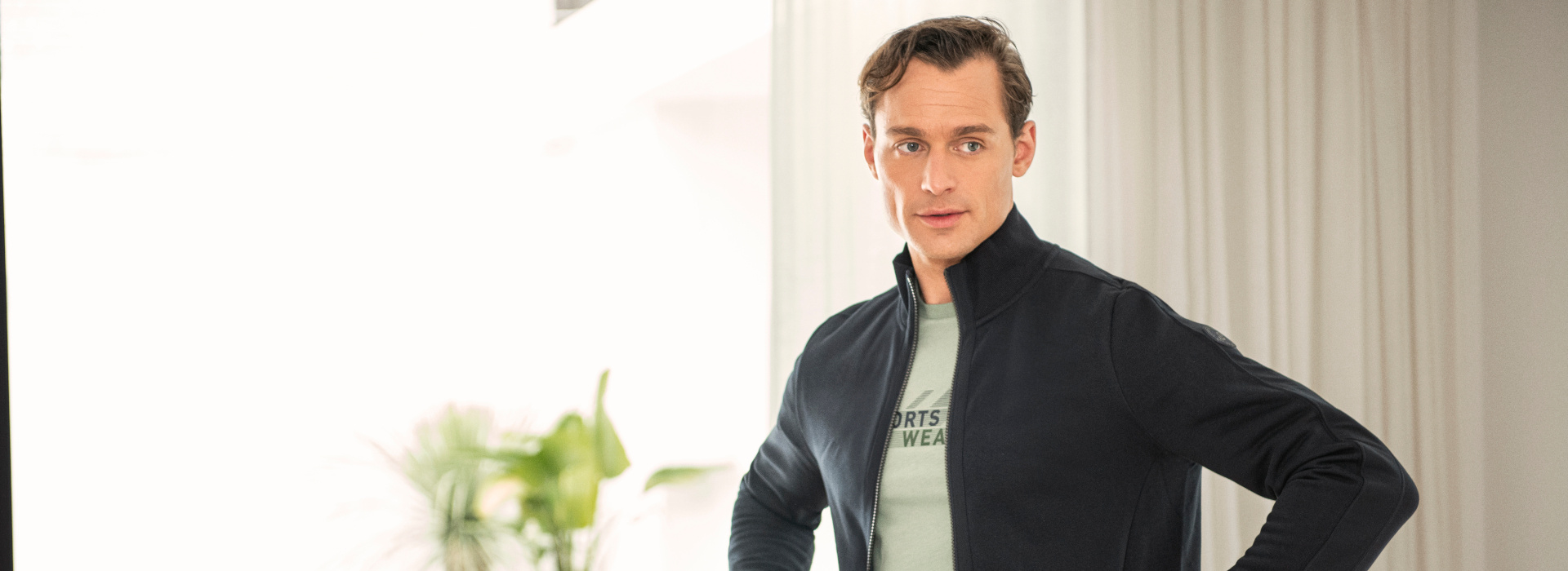 Mann in dunkelblauer Sweatjacke und mintfarbenem T-Shirt der Marke JOY sportswear.